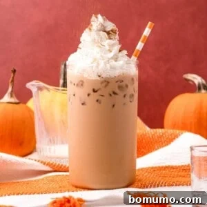 Iced pumpkin spice latte topped with whipped cream, against an inviting orange background.