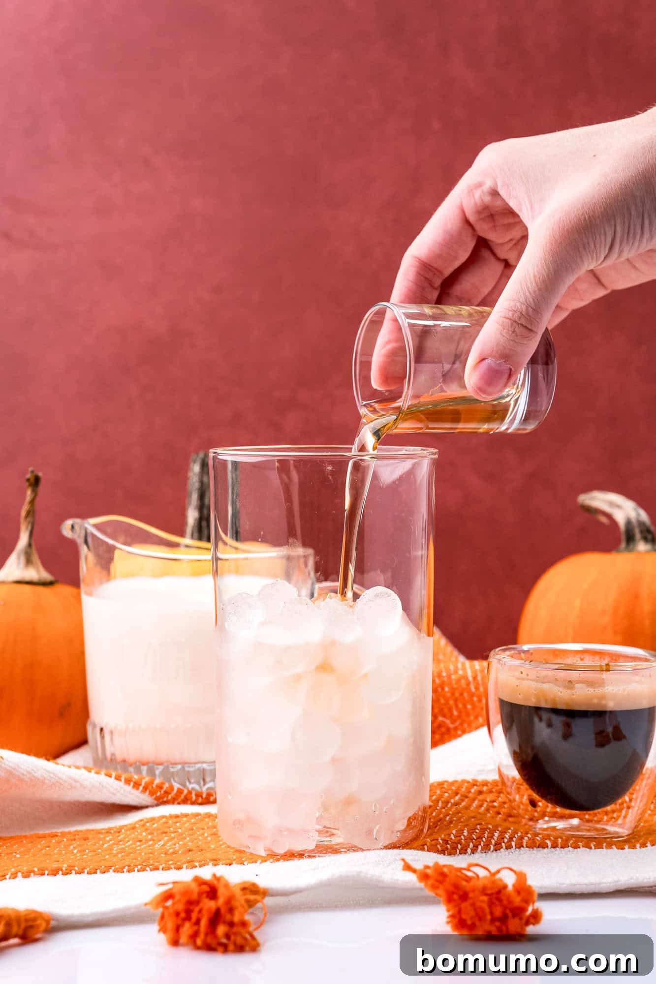 Pumpkin spice syrup being added to ice cubes in a clear glass, creating the flavor base for an iced latte.