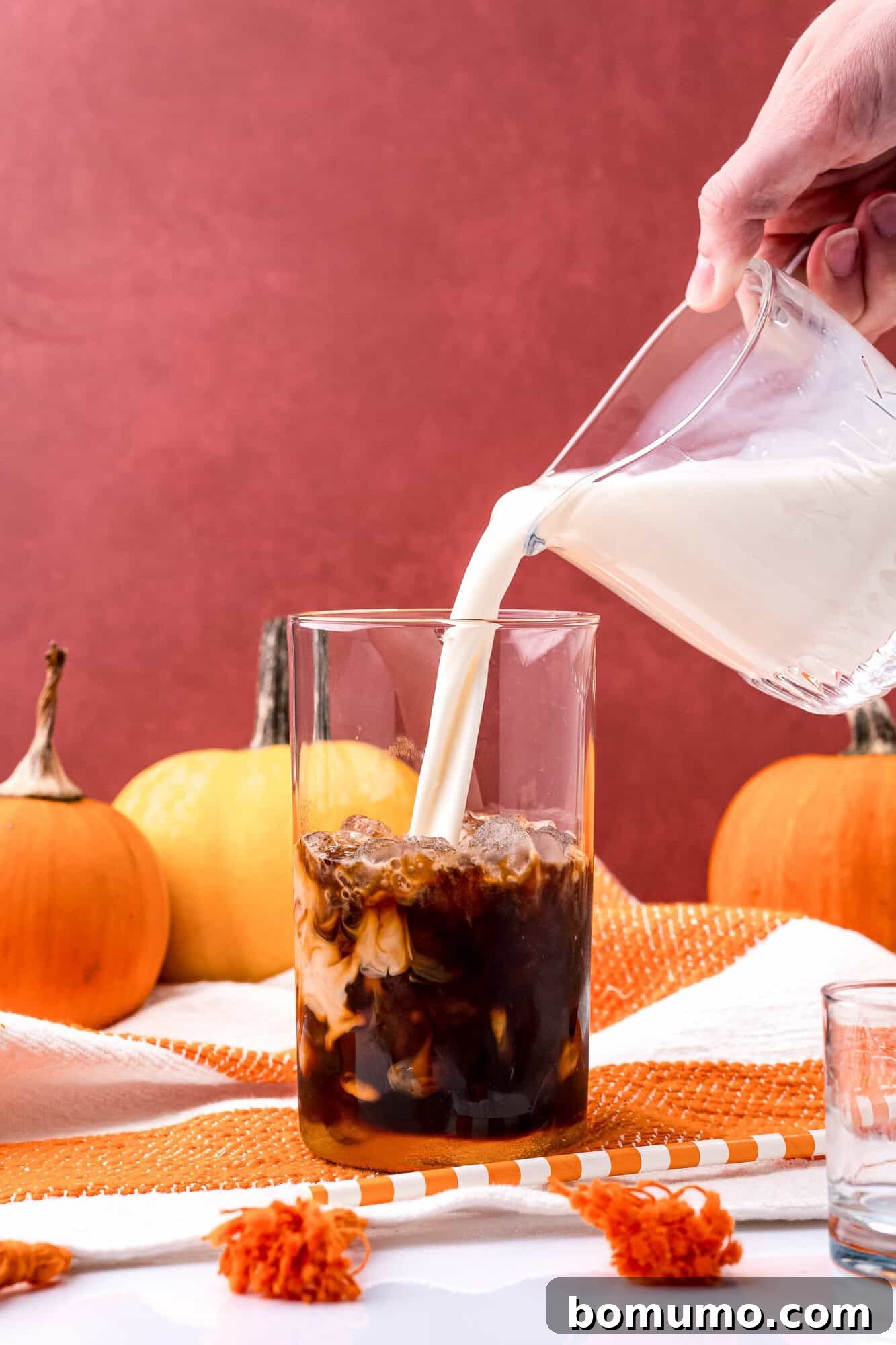 Milk being gently poured into the glass with ice and espresso, beginning to mix for a smooth iced latte.