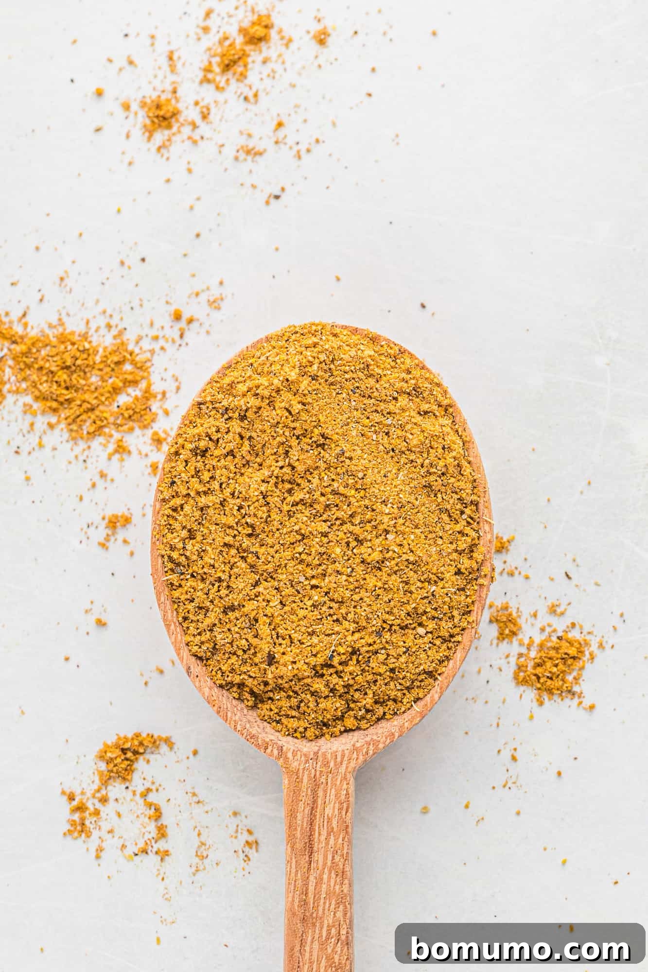 Homemade curry powder artfully arranged on a wooden spoon against a white background.