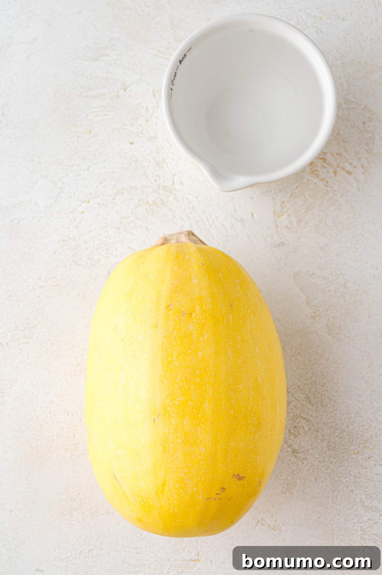 Easy Instant Pot Spaghetti Squash 4 Spaghetti squash and small cup of water, on a white surface.