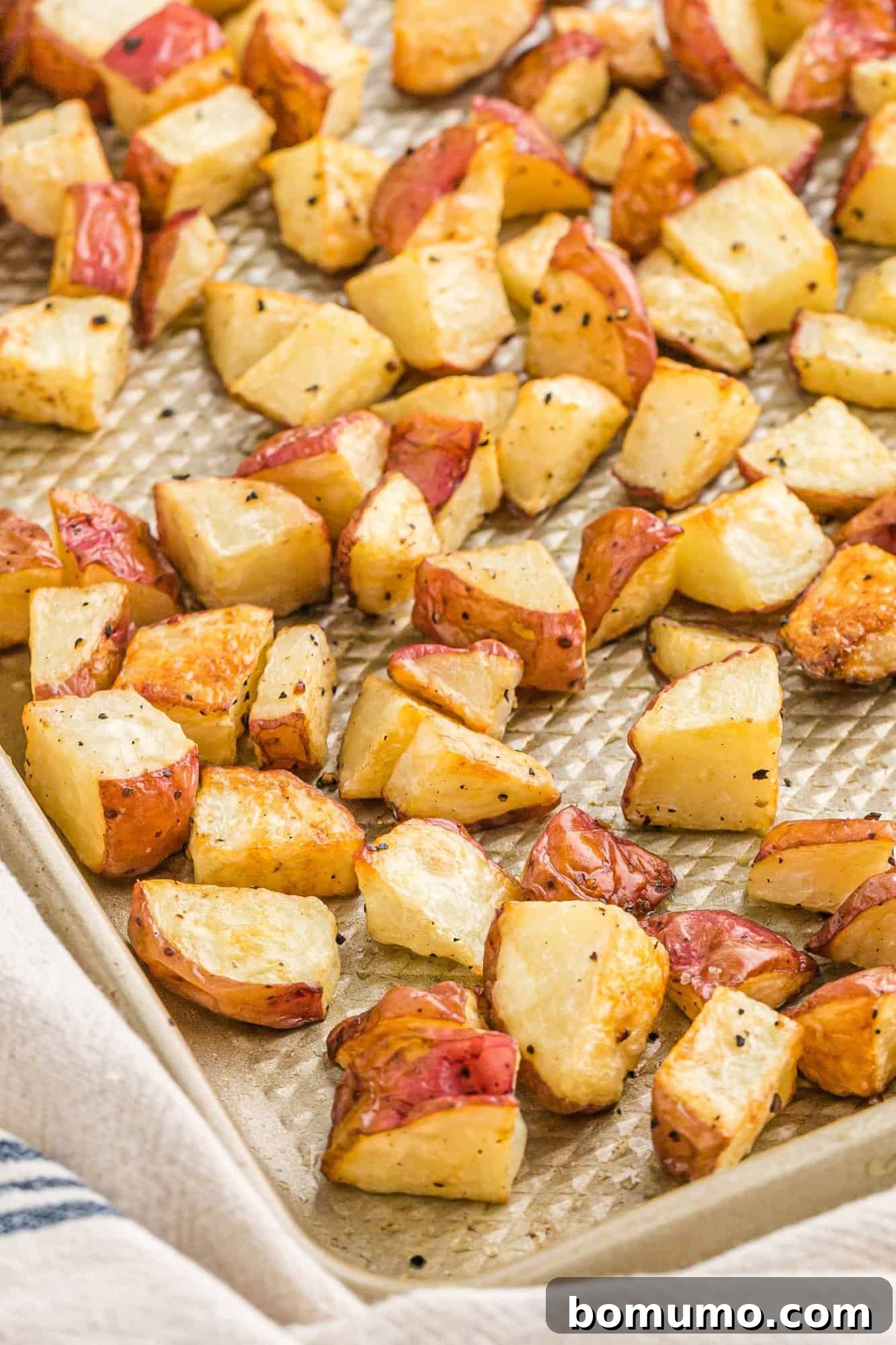 Close up of roasted potatoes arranged neatly on a sheet pan, showing their crispy texture and golden-brown skin.