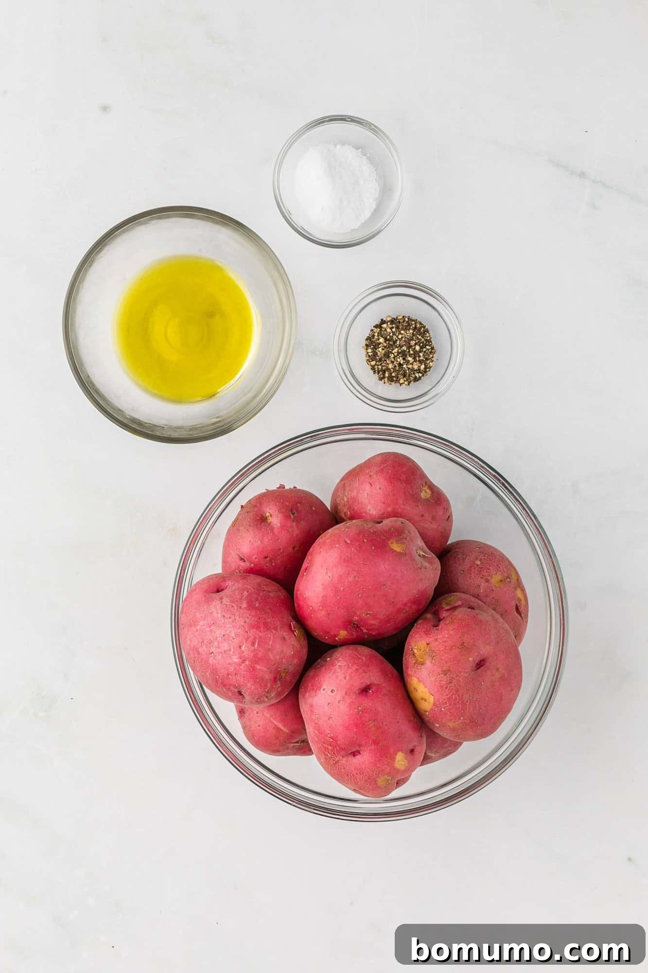 Essential ingredients for making crispy roasted potatoes laid out on a clean surface: red skin potatoes, olive oil, kosher salt, and coarse black pepper.