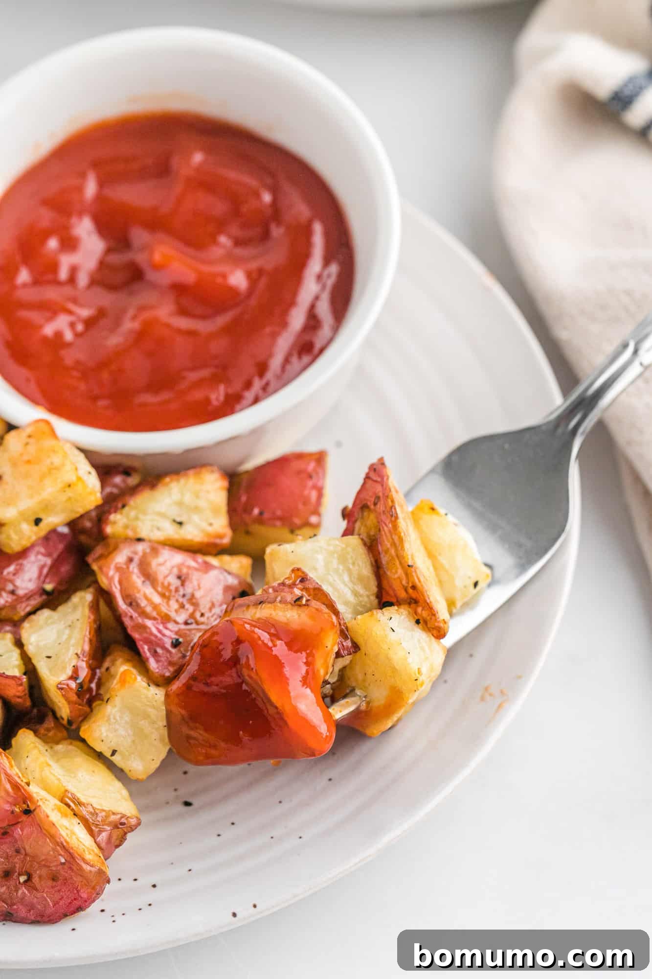 A plate of perfectly crispy roasted potatoes served with a side of ketchup, ready to be enjoyed.