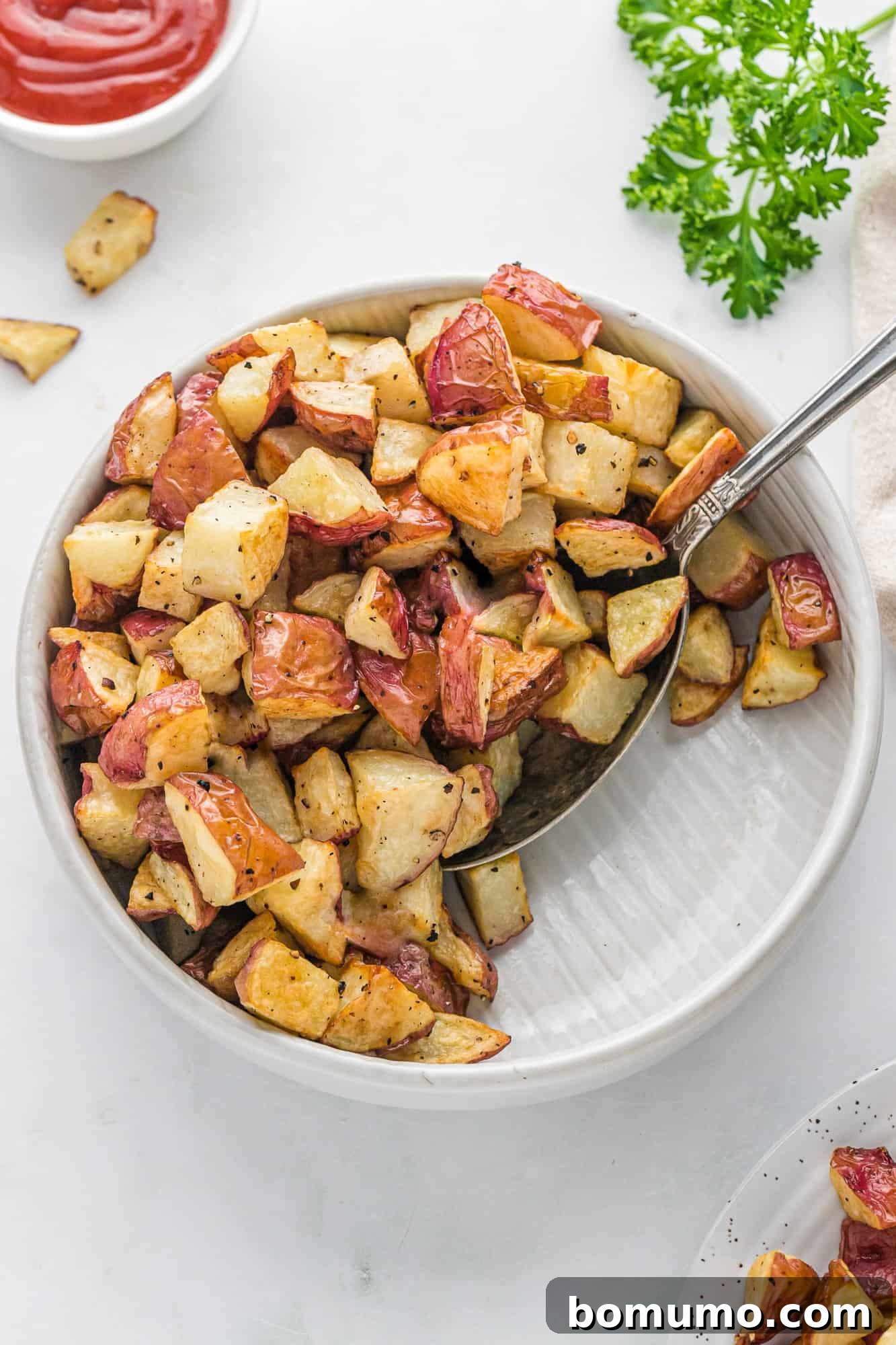 A large white serving bowl filled with freshly cooked crispy roasted potatoes, ready to be enjoyed.