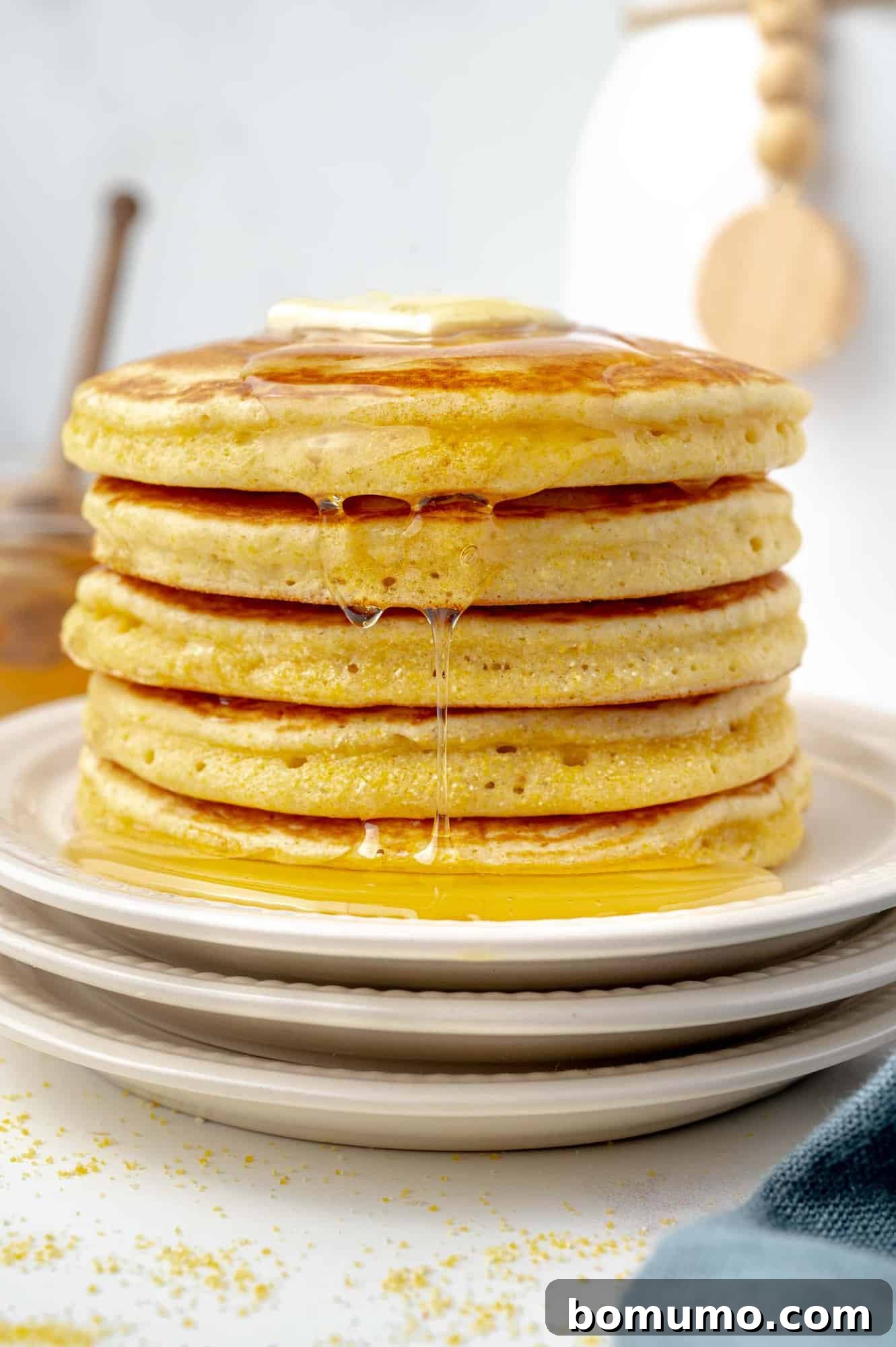 A glorious stack of golden cornbread pancakes, generously topped with a pat of melting butter and glistening with a sweet honey drizzle, stands proudly on a pristine white plate, ready to be enjoyed.