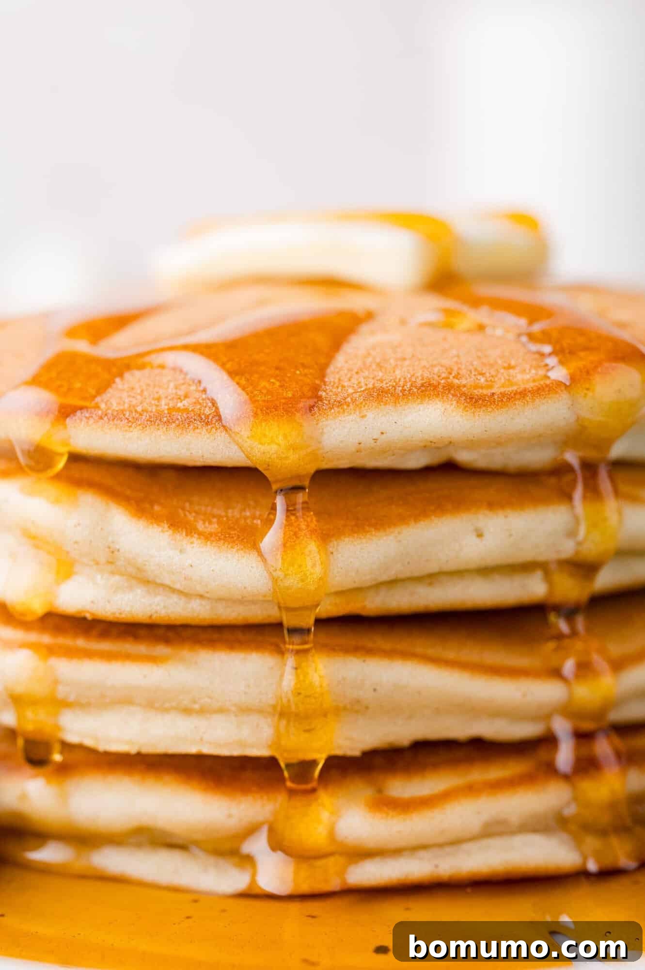A mouth-watering close-up of a towering stack of perfectly fluffy sweet cream pancakes, with luscious golden syrup cascading gracefully down their sides, promising a truly decadent bite.