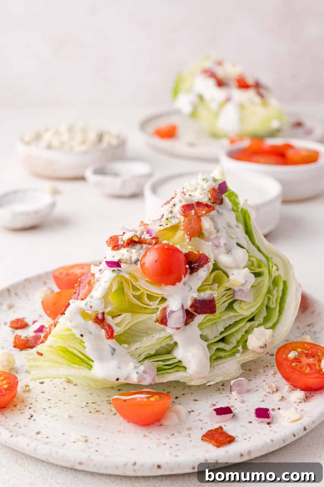 A beautifully plated wedge salad featuring crisp iceberg lettuce, vibrant cherry tomatoes, crumbled bacon, finely diced red onion, generous blue cheese crumbles, and a rich, creamy dressing drizzled over the top.