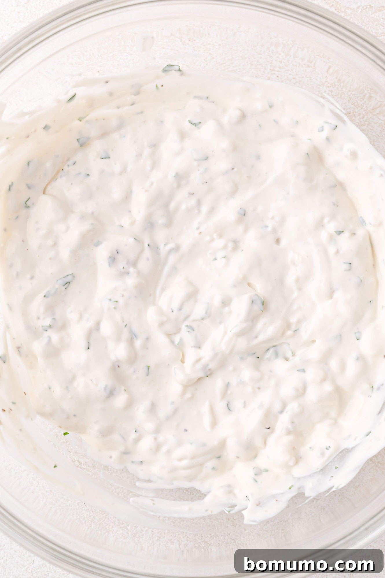 A clear bowl showcasing a thick, creamy blue cheese dressing, visibly speckled with vibrant green herbs, ready for serving.