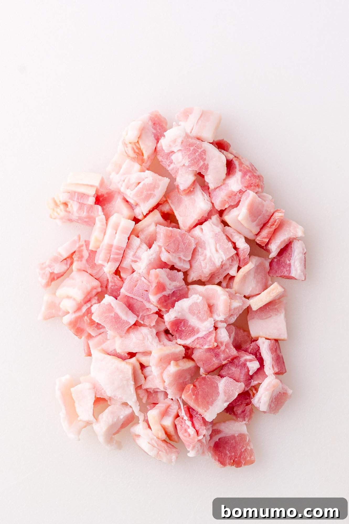 Small, uniformly chopped pieces of raw bacon laid out on a clean white surface, ready for cooking.