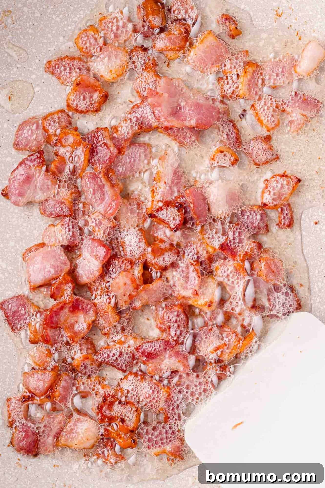 A close-up shot of small, crispy bacon pieces sizzling dynamically in a hot pan, with visible grease and small bubbles indicating perfect cooking.