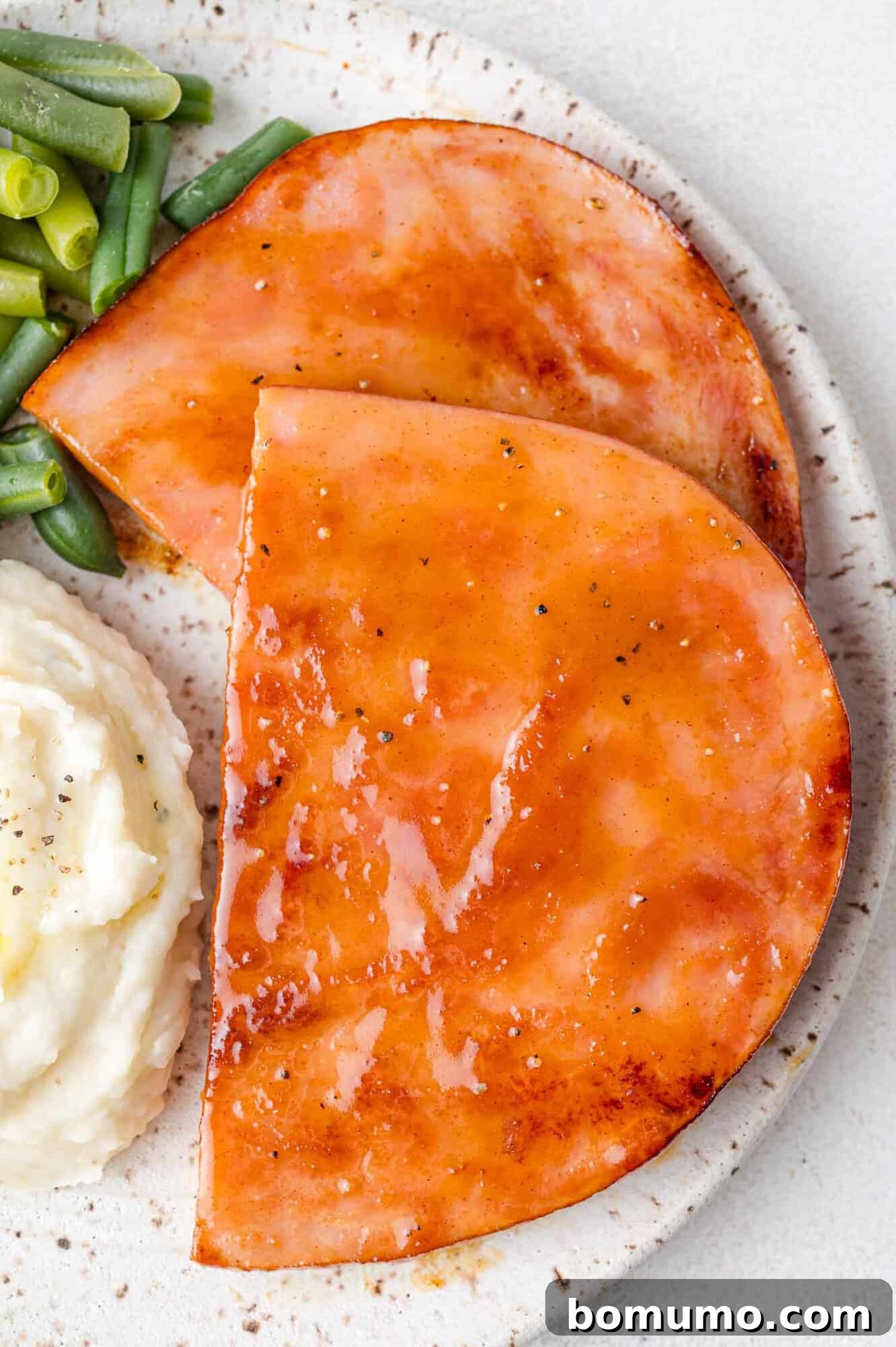 Sliced ham with a sweet and savory glaze, beautifully plated with creamy mashed potatoes and vibrant green beans, ready to be served.