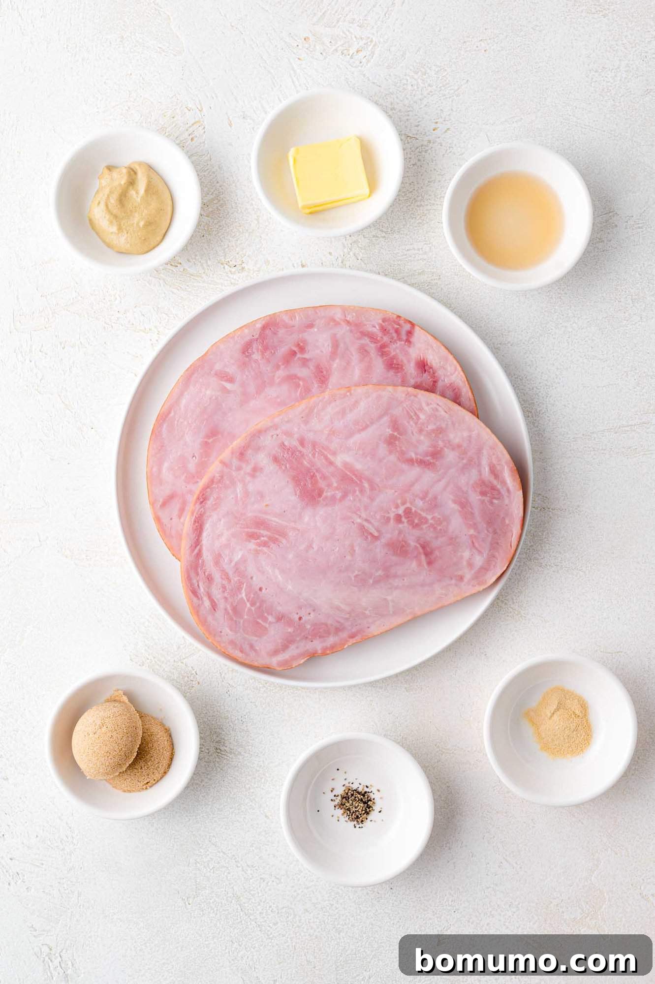 A neatly arranged plate showcases two slices of ham, surrounded by small, pristine bowls containing an array of fresh ingredients: vibrant mustard, rich butter, tangy vinegar, sweet brown sugar, fragrant black pepper, and a powdered spice blend. All are artfully displayed on a light, textured surface, hinting at the culinary journey ahead.