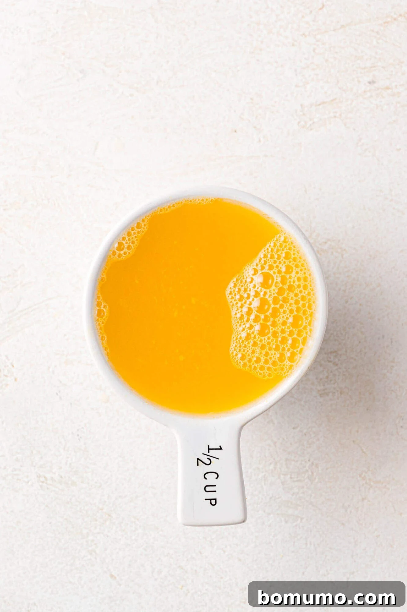 Vibrant Cranberry Orange Compote 5 A white measuring cup labeled 1/2 cup filled with vibrant orange juice, on a textured white surface, showing the prepared liquid ingredient.