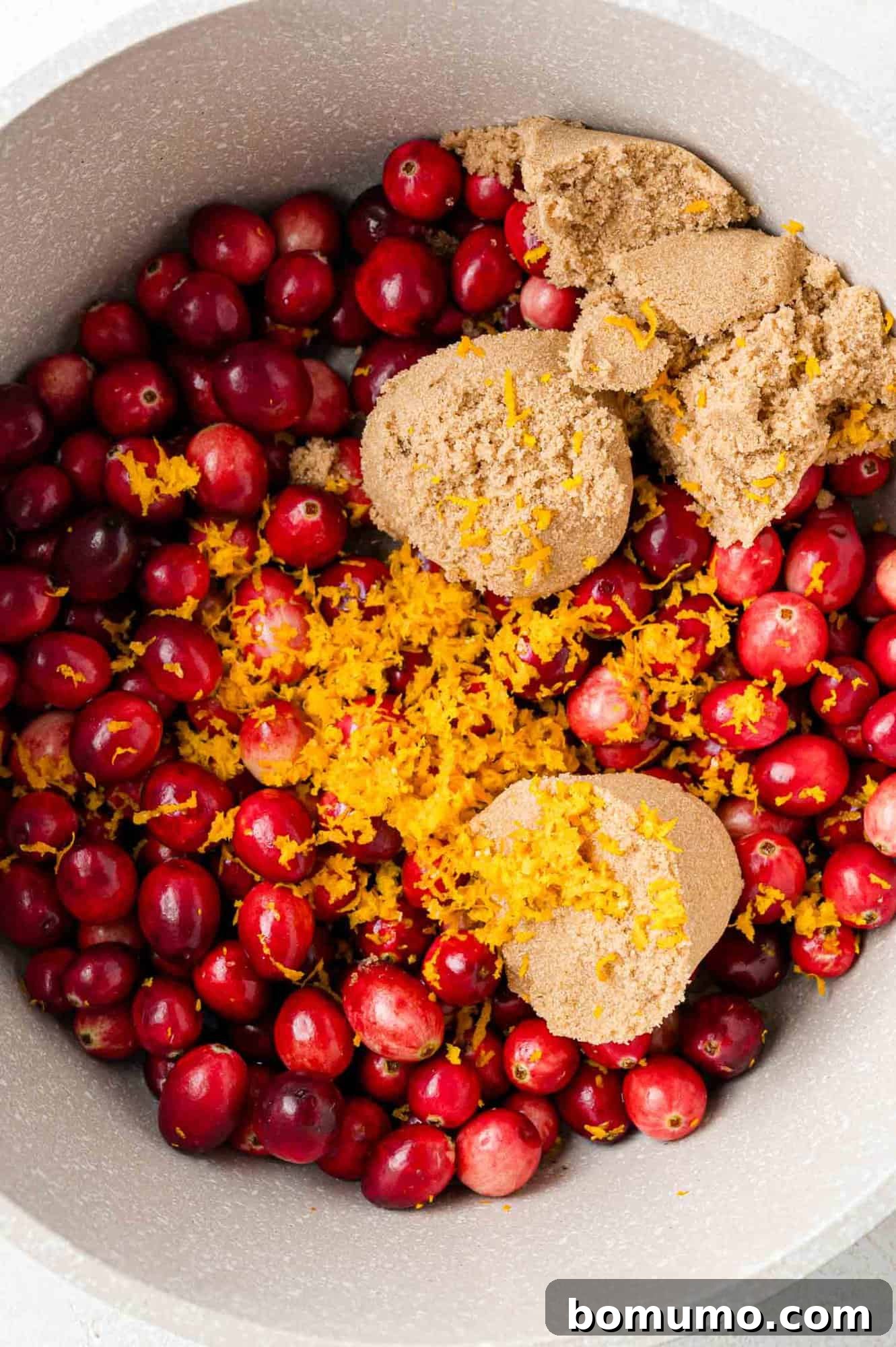 Vibrant Cranberry Orange Compote 8 A bowl filled with fresh cranberries, topped with brown sugar and orange zest, illustrating the initial combination of ingredients.