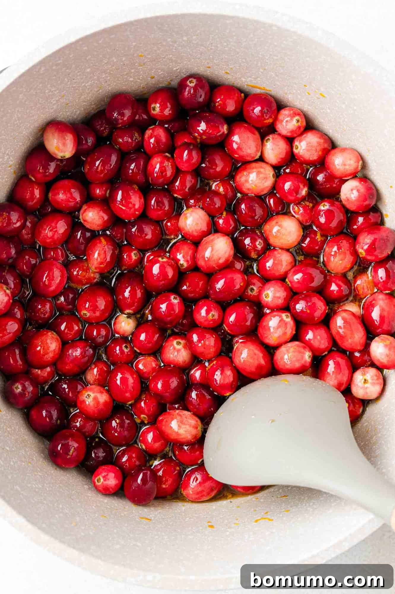 Vibrant Cranberry Orange Compote 9 A pot filled with fresh cranberries being stirred with a gray spatula, showing the early stages of cooking.