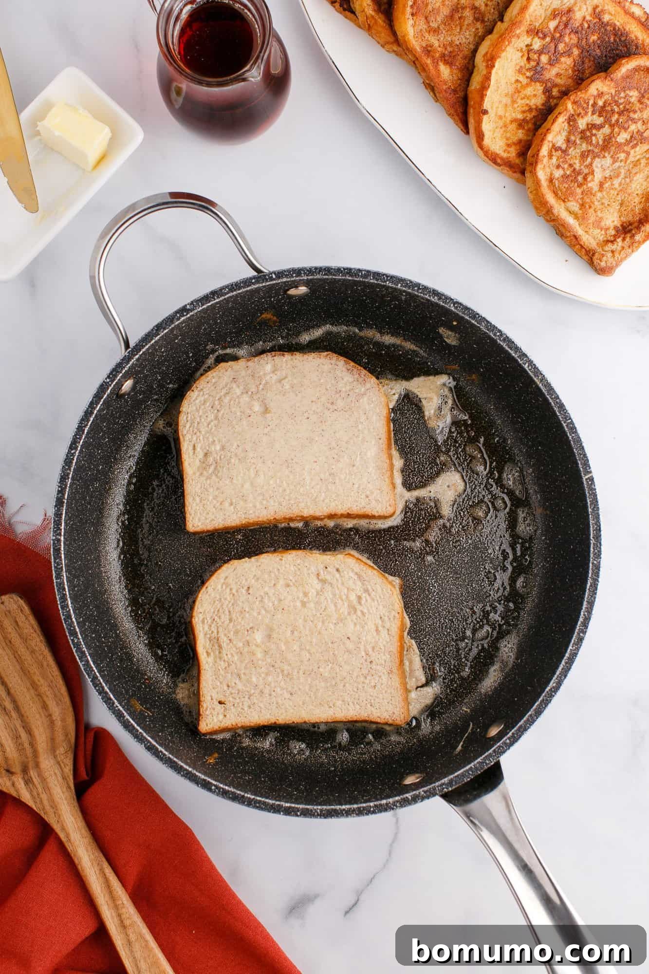 Two slices of bread frying in a black skillet, with melted butter around them.