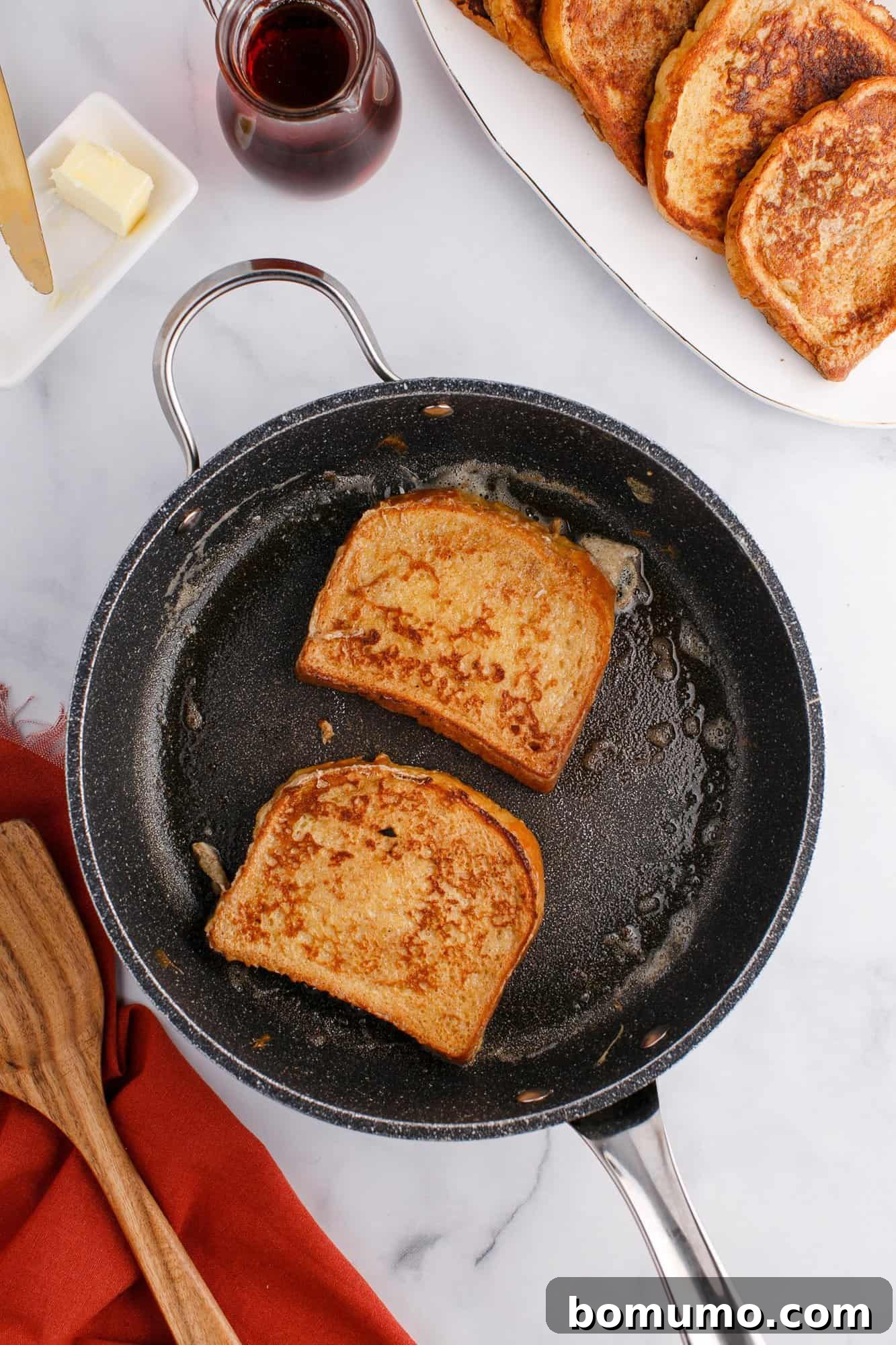Two slices of French toast cooking in a black skillet.