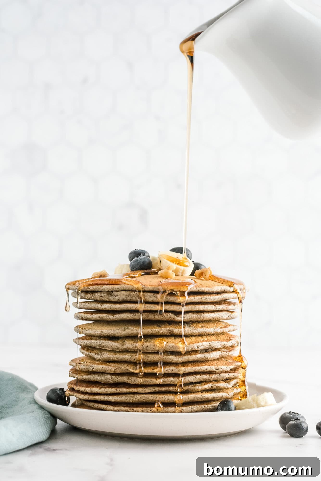 Tall stack of fluffy buckwheat pancakes topped with fresh blueberries and glistening maple syrup, ready to be enjoyed.