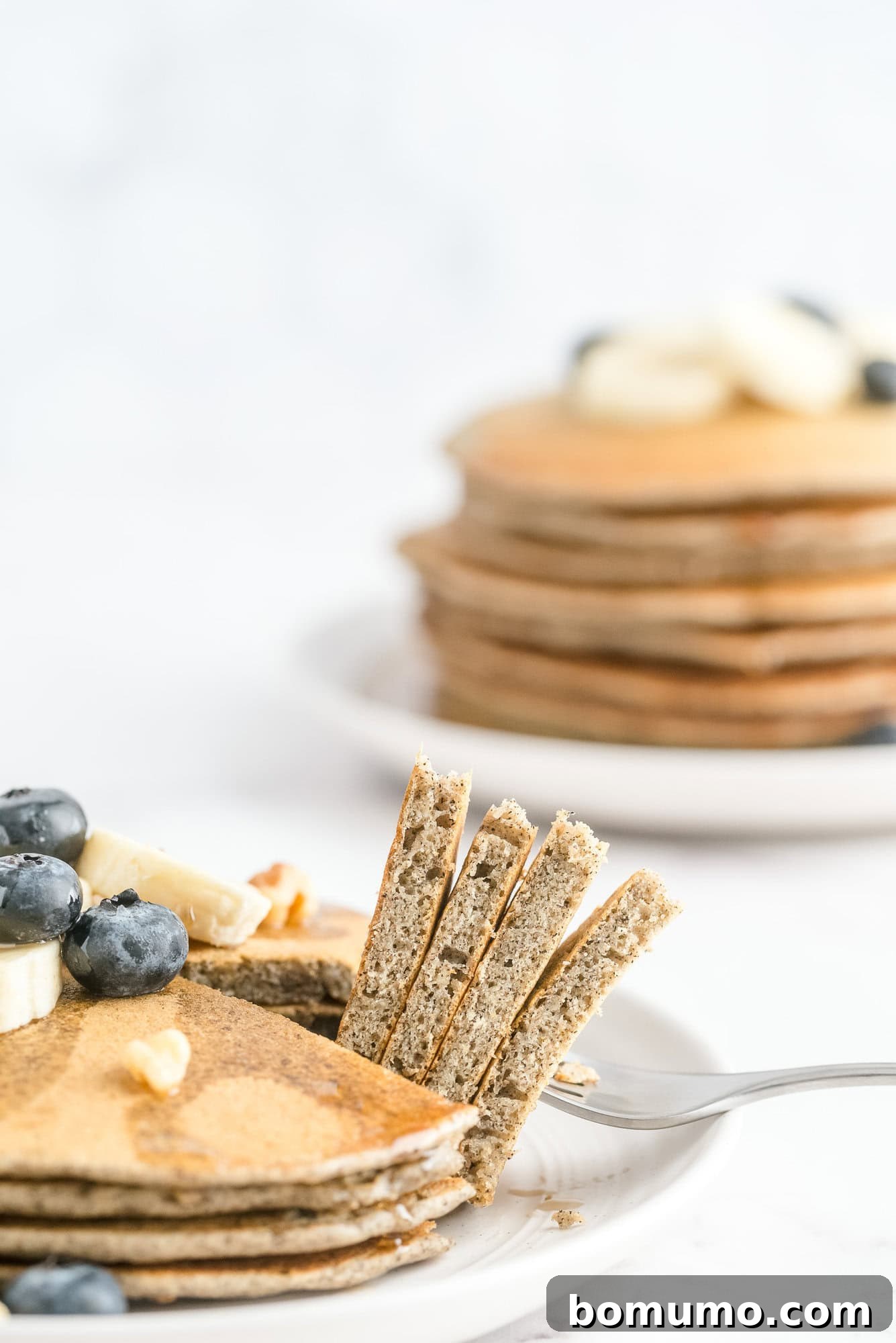 Two enticing stacks of freshly cooked buckwheat pancakes, one with a wedge carefully cut and lifted by a fork, ready for a bite.