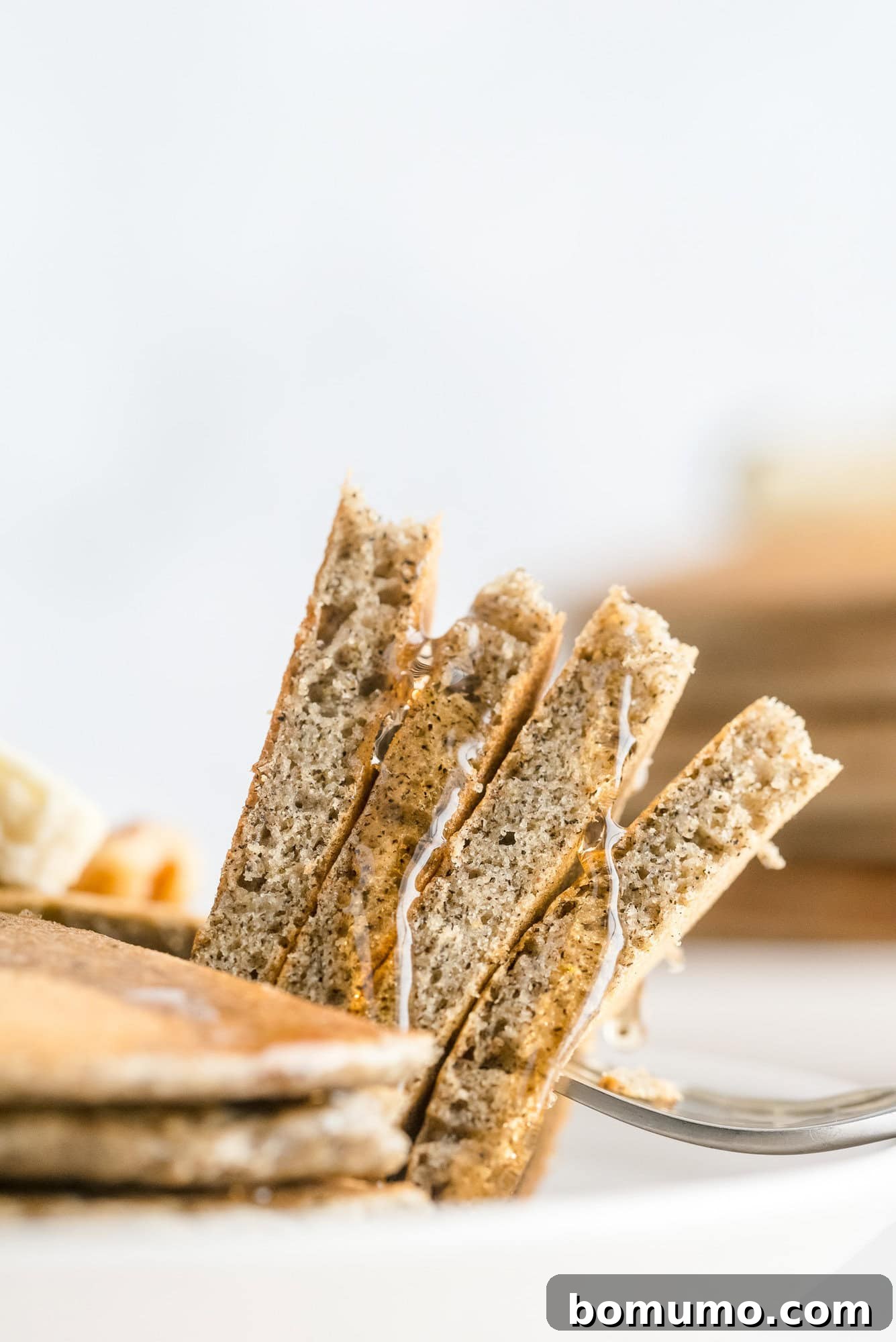 A perfectly cut wedge of a buckwheat pancake, drizzled with sweet syrup, delicately balanced on a fork.