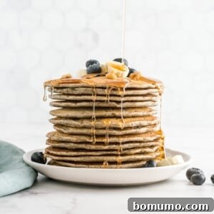 Tall stack of buckwheat pancakes topped with blueberries and maple syrup.