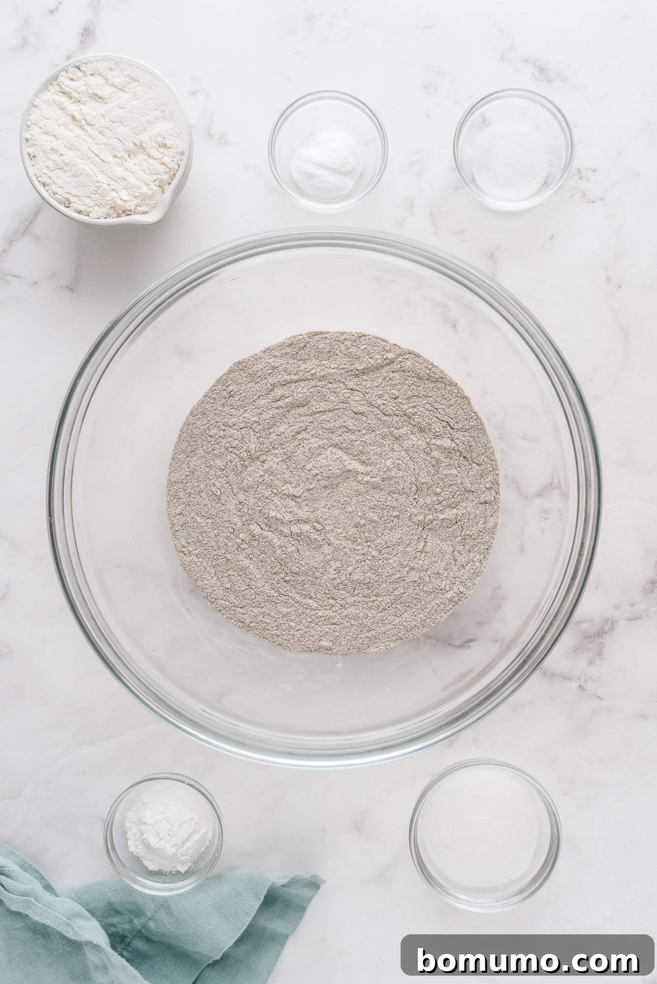 Separate clear glass bowls holding various dry ingredients like flour, sugar, and leavening agents for pancakes.