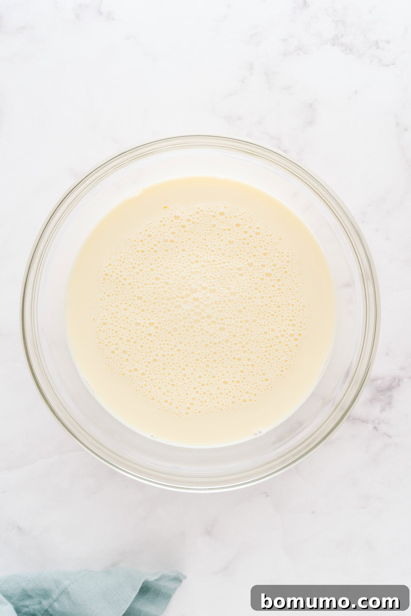 All wet ingredients, including milk, eggs, and vanilla, thoroughly combined in a large glass mixing bowl.