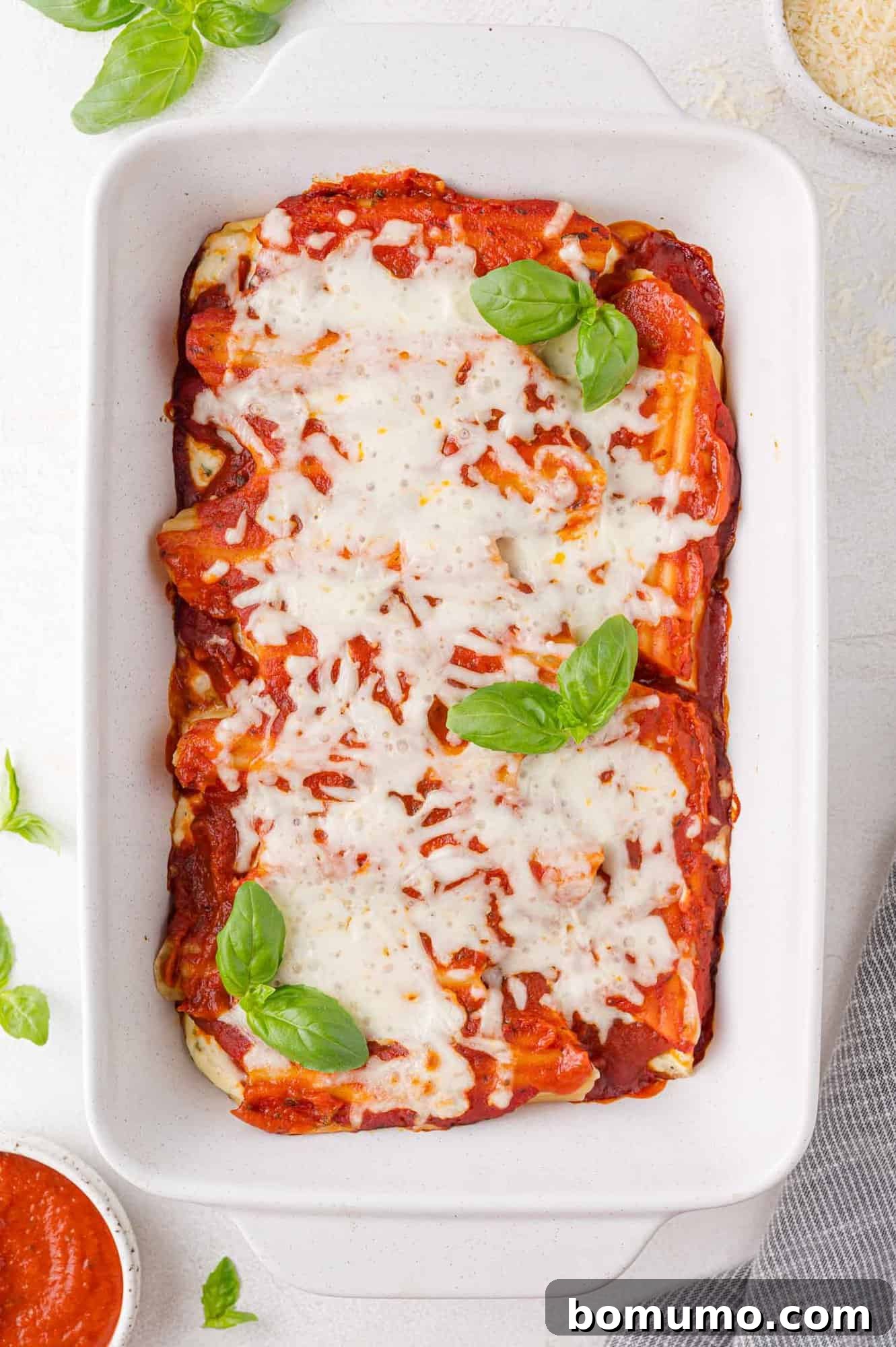Baked manicotti in a white dish topped with melted cheese and garnished with fresh basil leaves.
