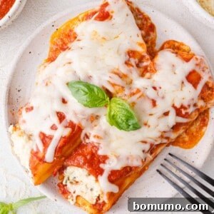 Plate of manicotti topped with tomato sauce, melted cheese, and basil leaves. Fork on the side.