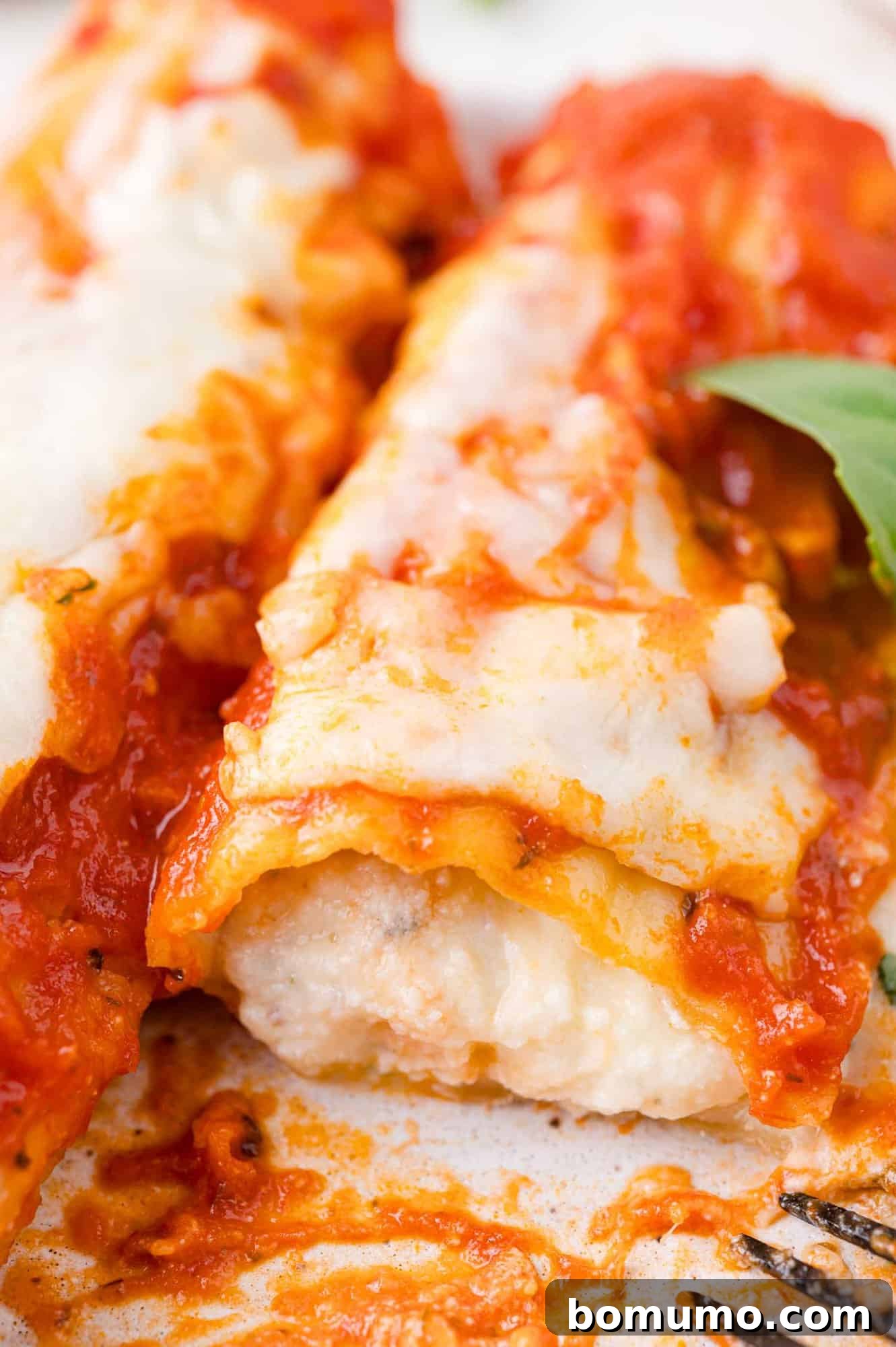 Close-up of manicotti topped with melted cheese and tomato sauce, garnished with a basil leaf.