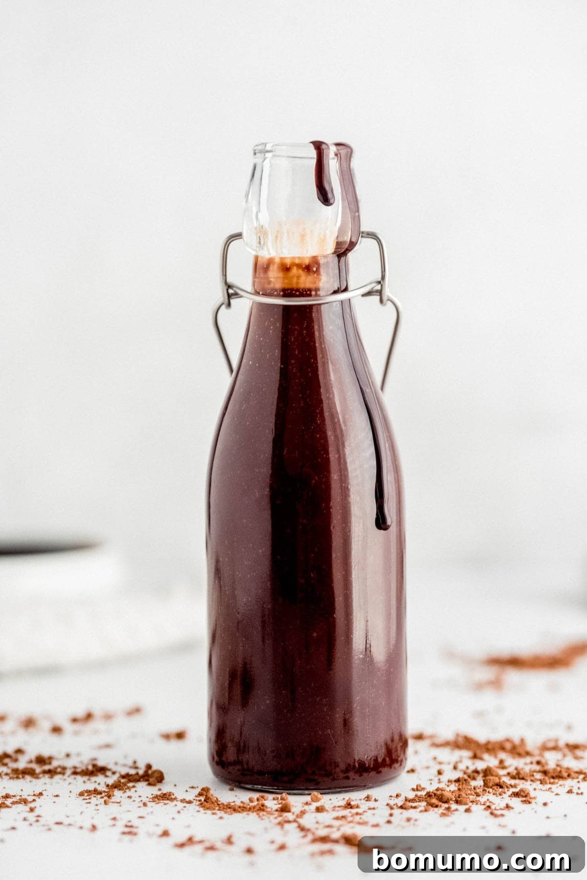 A glass bottle filled with rich, dark homemade chocolate syrup, secured with a classic swing-top cap, ready for use.