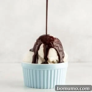 Creamy vanilla ice cream in a blue cup with rich chocolate syrup being generously poured on top, highlighting a perfect dessert topping.