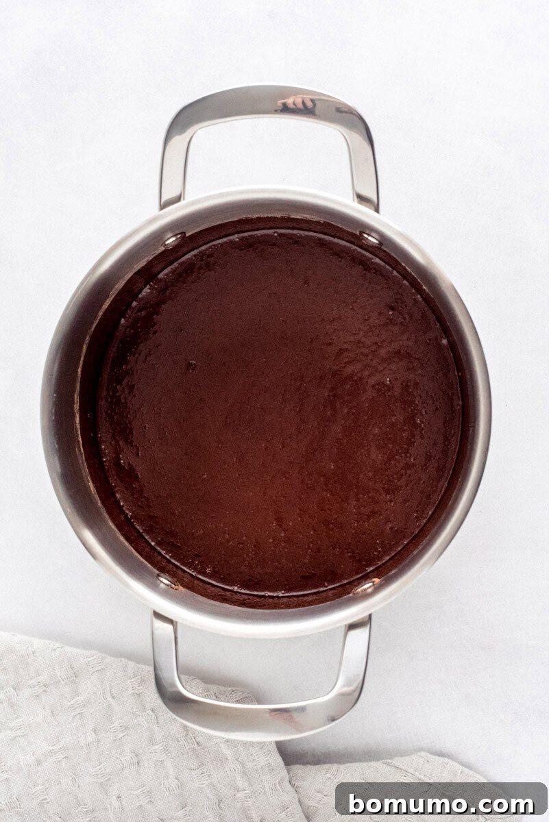 Chocolate syrup gently simmering in a stainless steel pan, showing a slightly thickened, glossy texture during the cooking process.