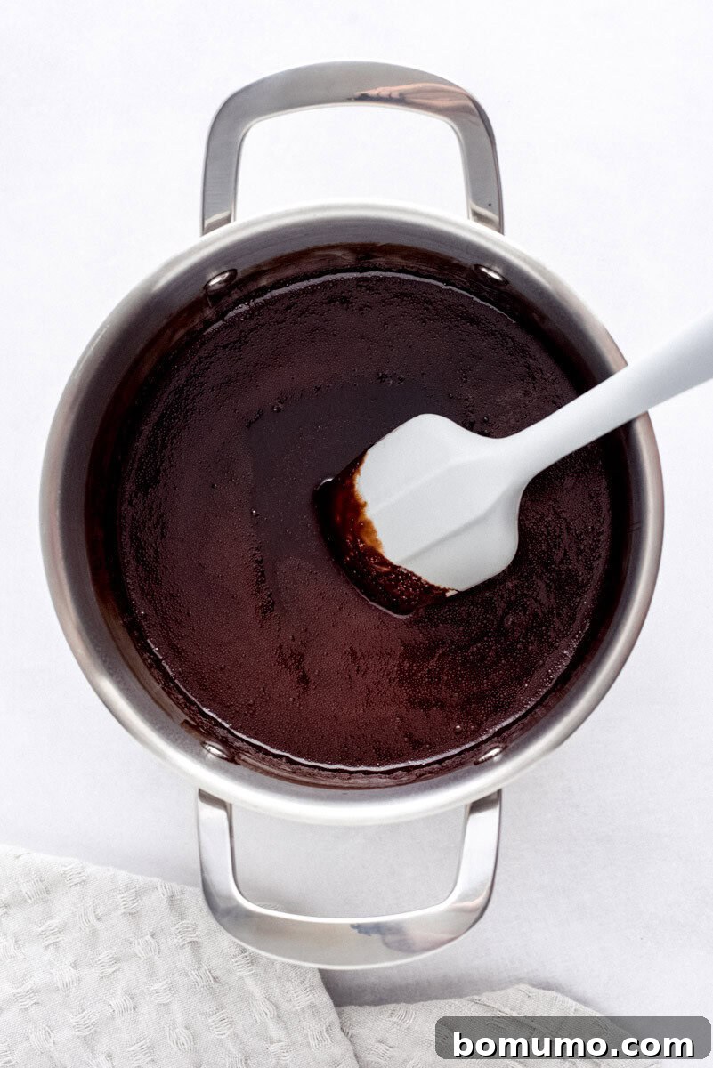A spatula stirring perfectly thickened chocolate syrup in a stainless steel pot, highlighting its rich, glossy texture before transfer.