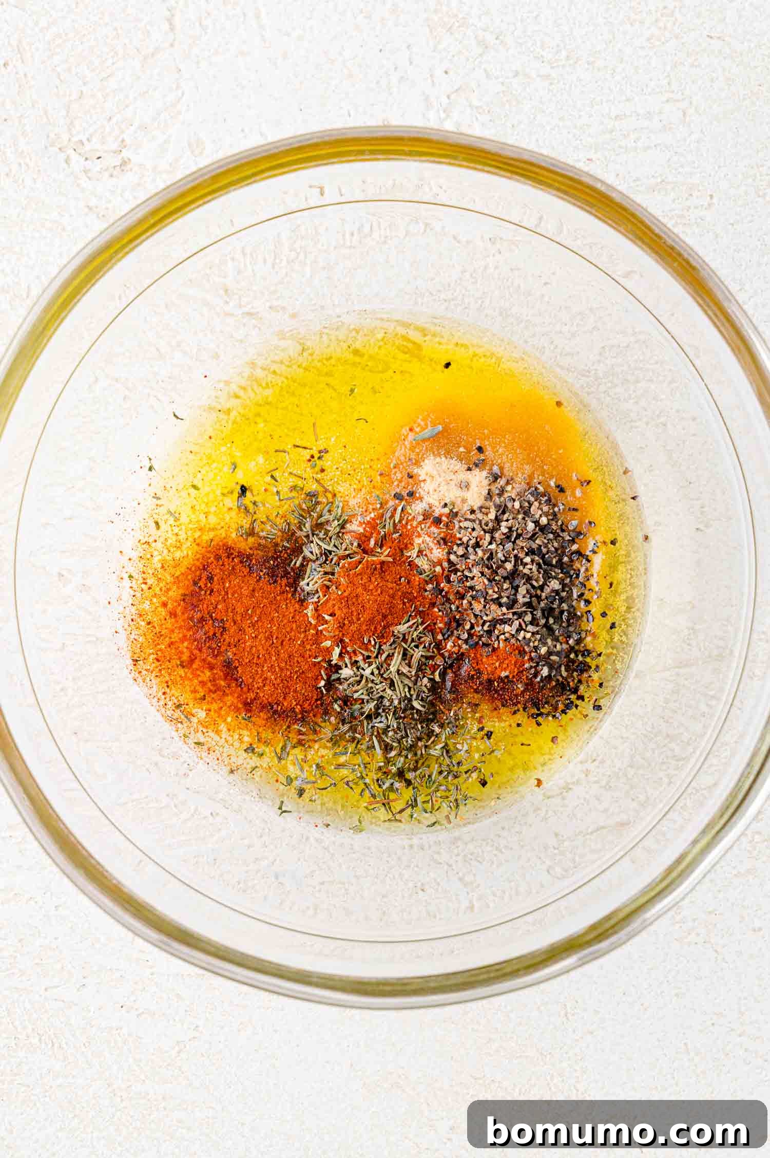 A glass bowl containing a mixture of spices including paprika, black pepper, and dried herbs on a white background.