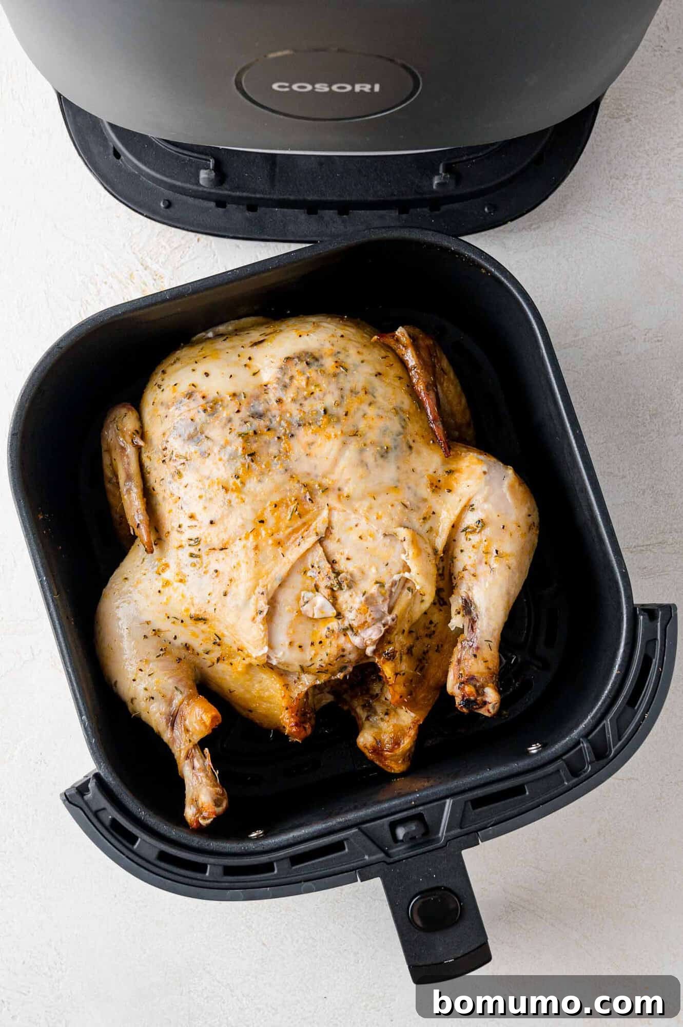A whole roasted chicken inside an air fryer basket, reflecting a golden brown finish. 