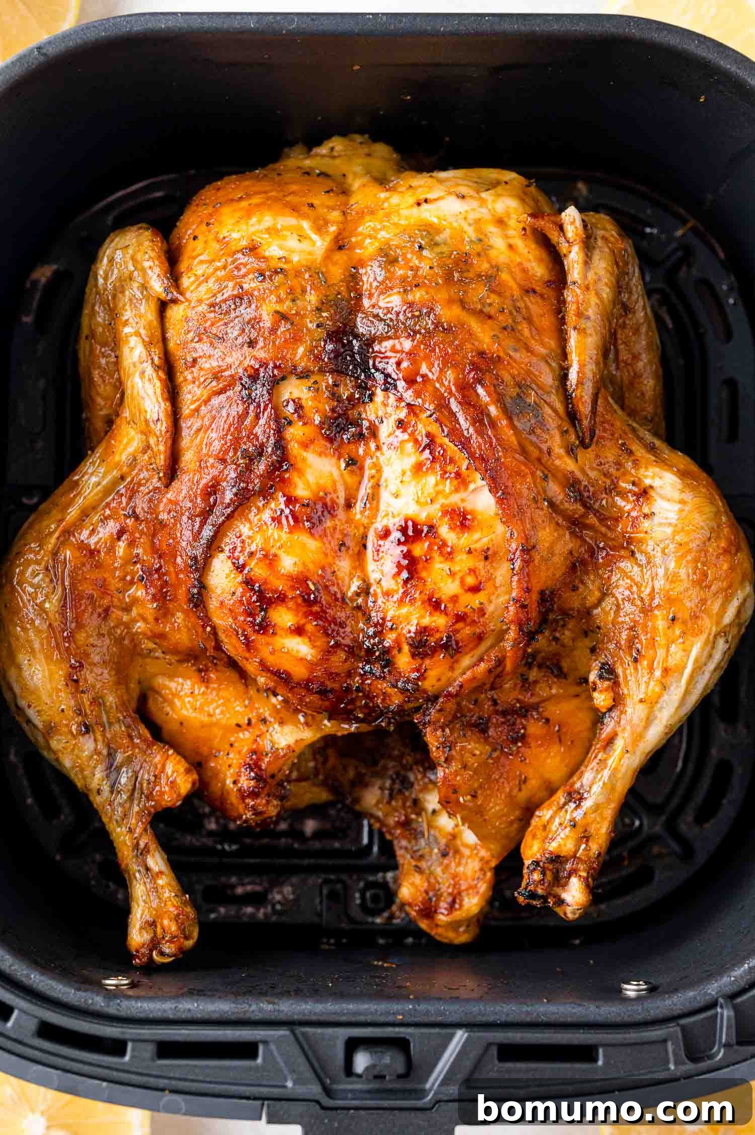 A whole roasted chicken with golden brown skin is placed in an air fryer basket.