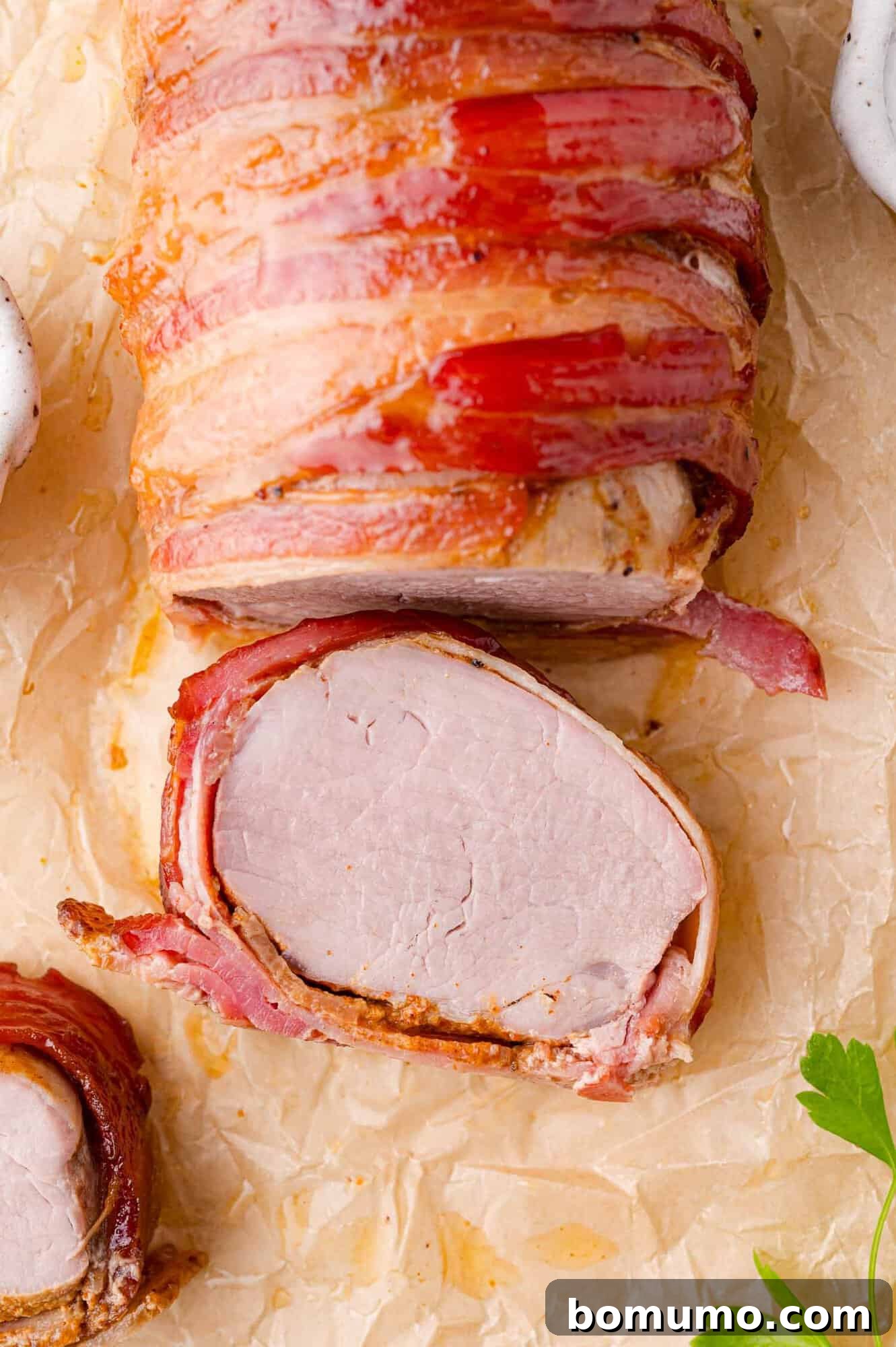 Bacon-wrapped pork tenderloin on parchment, sliced to reveal the interior.