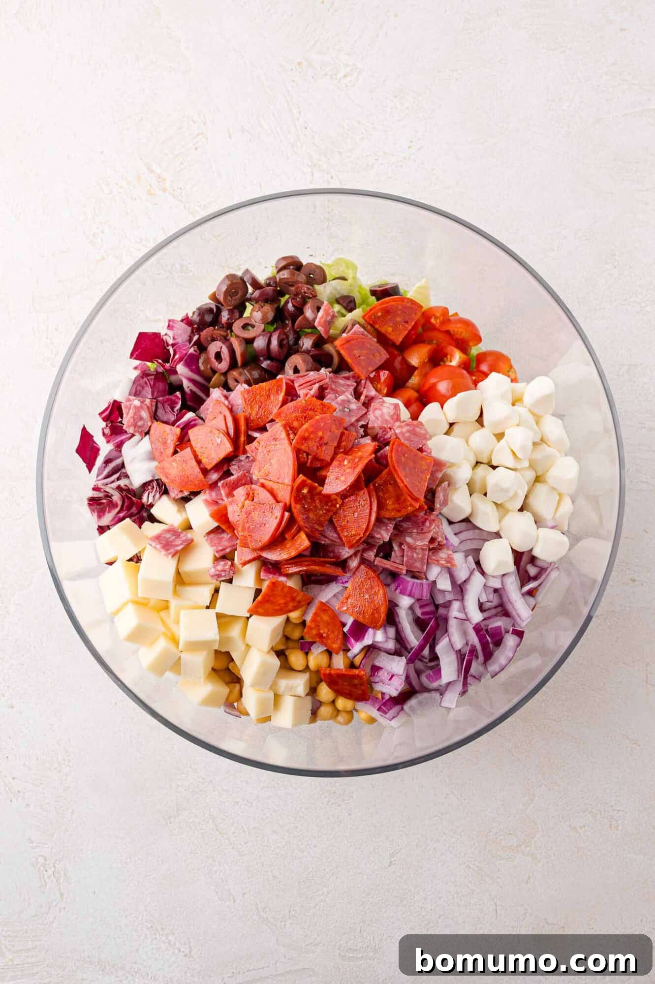 Chopped Salad Perfection 5 A bowl of assorted chopped salad ingredients including pepperoni, cheese cubes, olives, onions, tomatoes, and mozzarella balls.