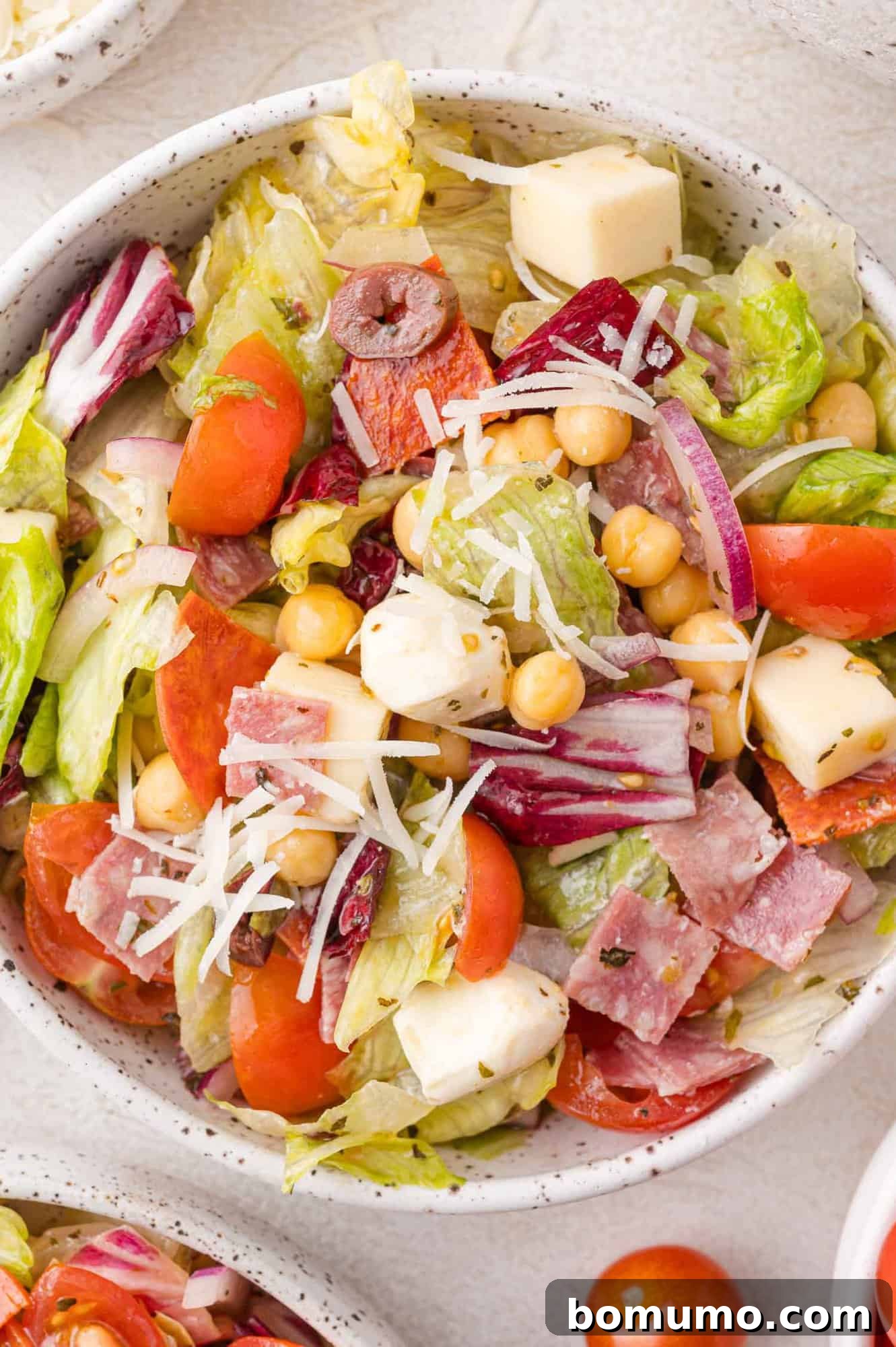 Chopped Salad Perfection 10 A bowl of salad containing lettuce, cherry tomatoes, red onion, chickpeas, mozzarella cubes, olives, salami, and shredded cheese.