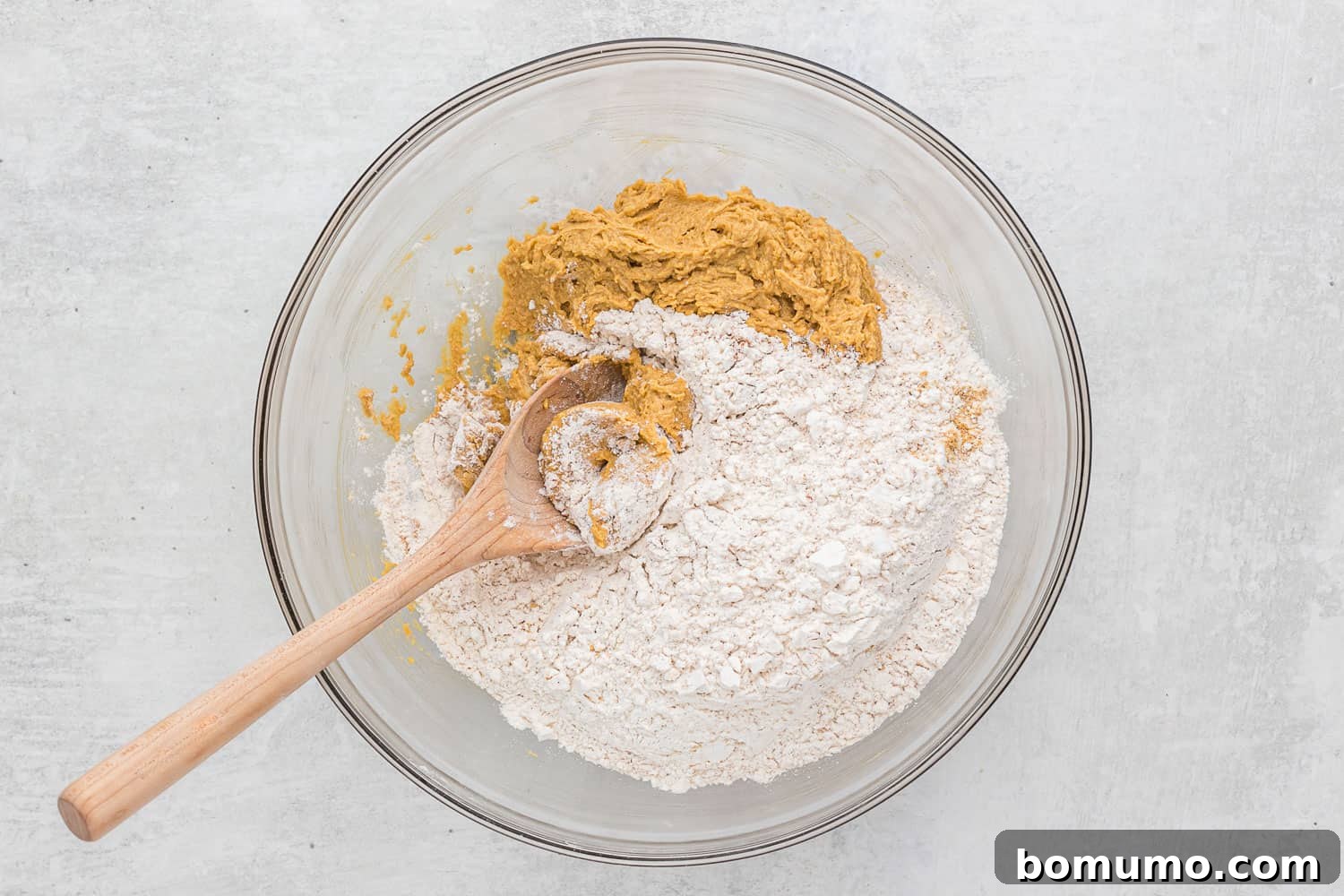 Dry ingredients, including flour and spices, piled on top of the wet ingredients in a mixing bowl, prior to being blended into cookie dough.