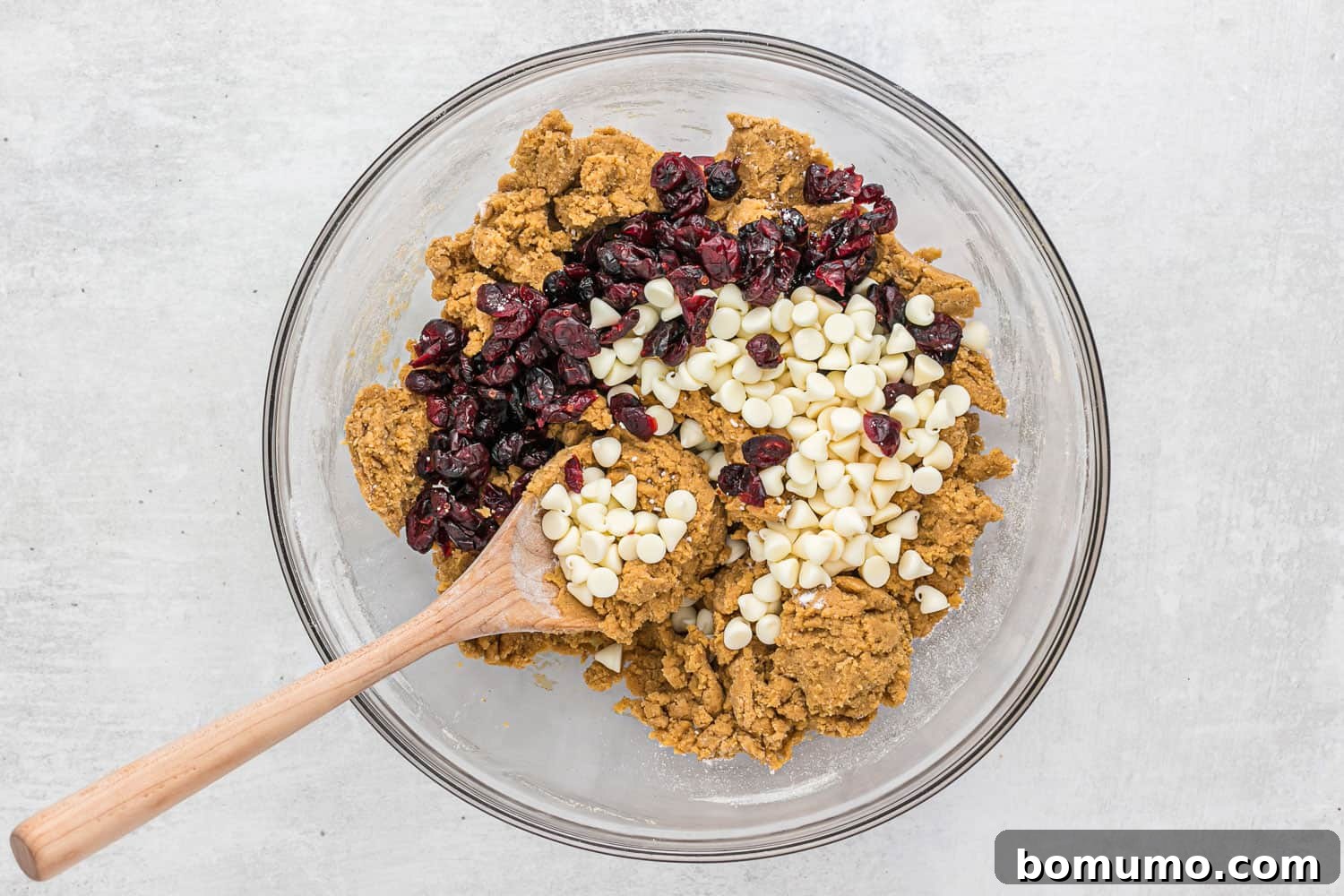 White chocolate chips and dried cranberries resting on top of the prepared cookie dough in a bowl, awaiting their final mix-in.