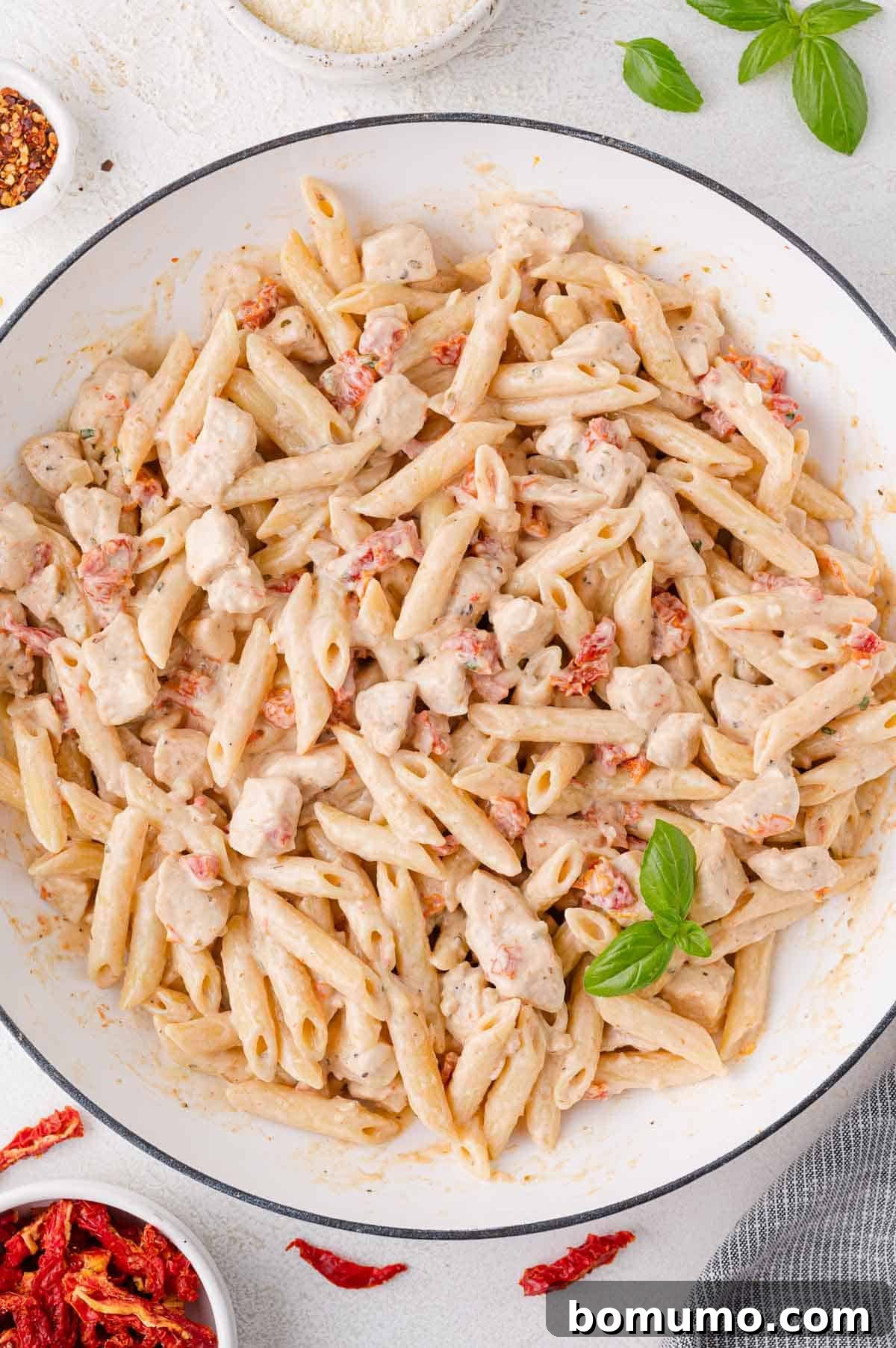 A pan of rich, creamy penne pasta with succulent chicken pieces, vibrant sun-dried tomatoes, and a fresh basil garnish, ready to be served.