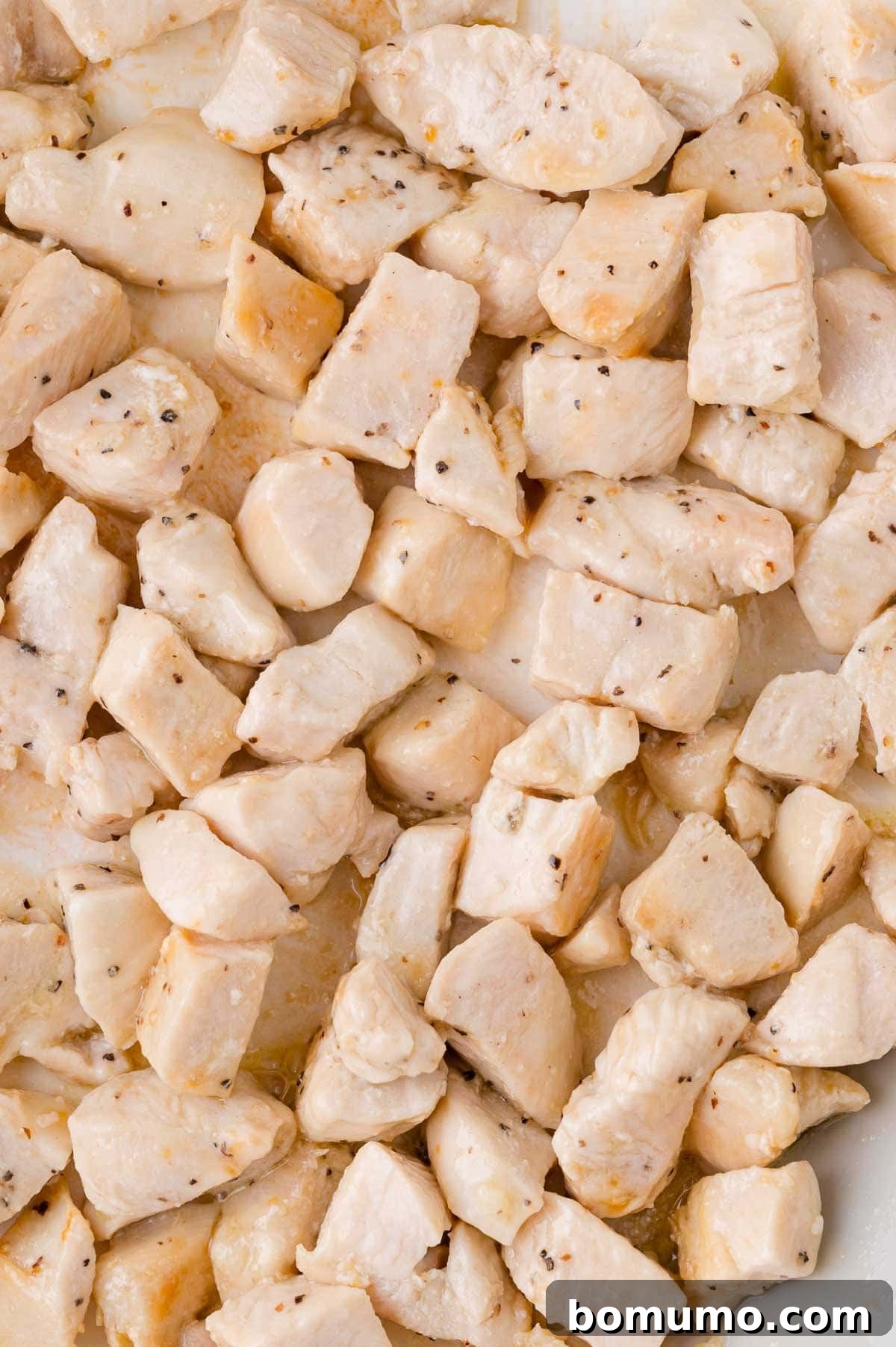 Close-up of cooked diced chicken pieces, beautifully browned and seasoned with pepper, resting in a skillet.