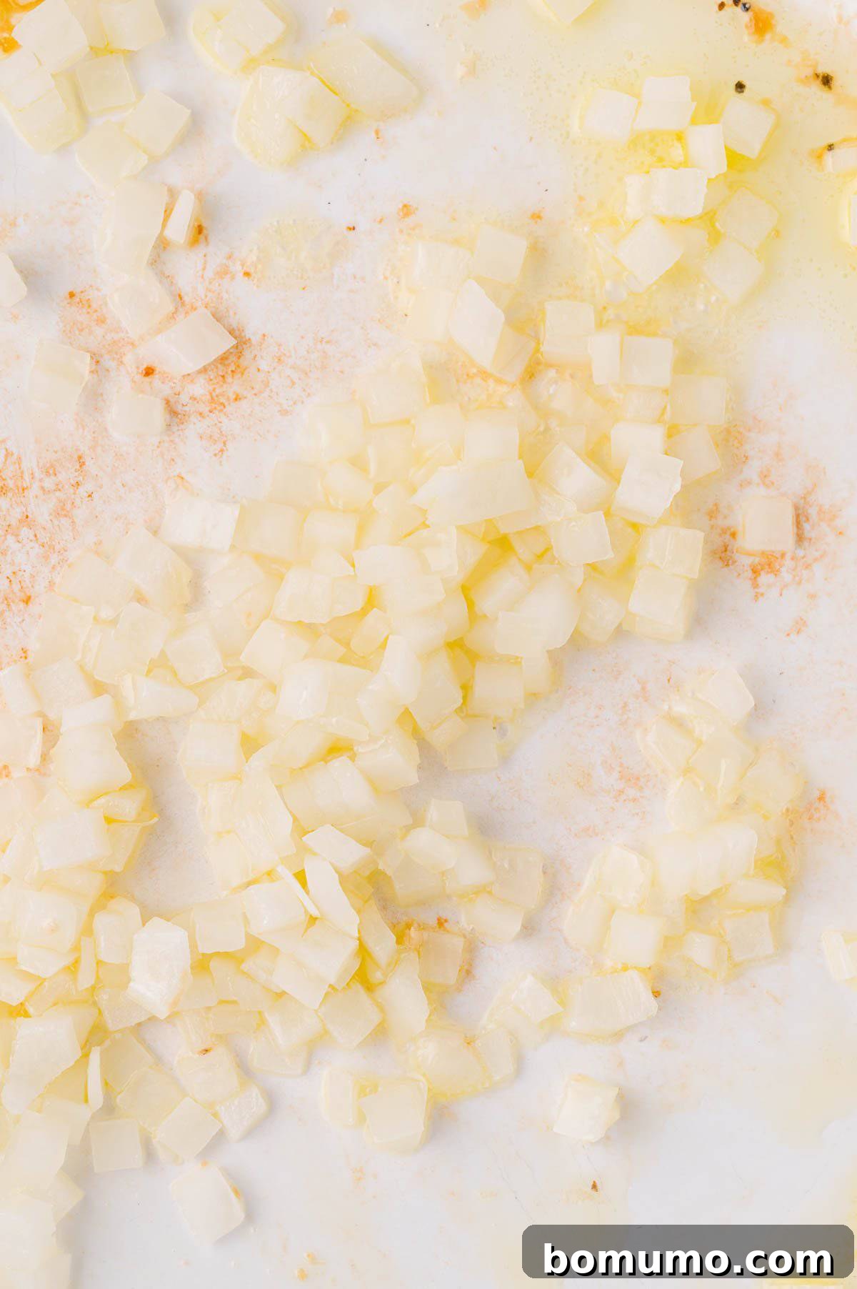 Finely diced onions gently sautéing in a large frying pan, translucent and fragrant.