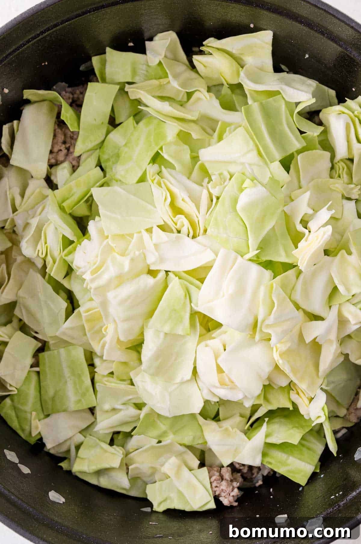 Deconstructed Cabbage Roll Soup 7 A close-up shot of freshly chopped green cabbage pieces, neatly gathered in a deep black pot, poised to be cooked into a delicious and tender component of the soup.
