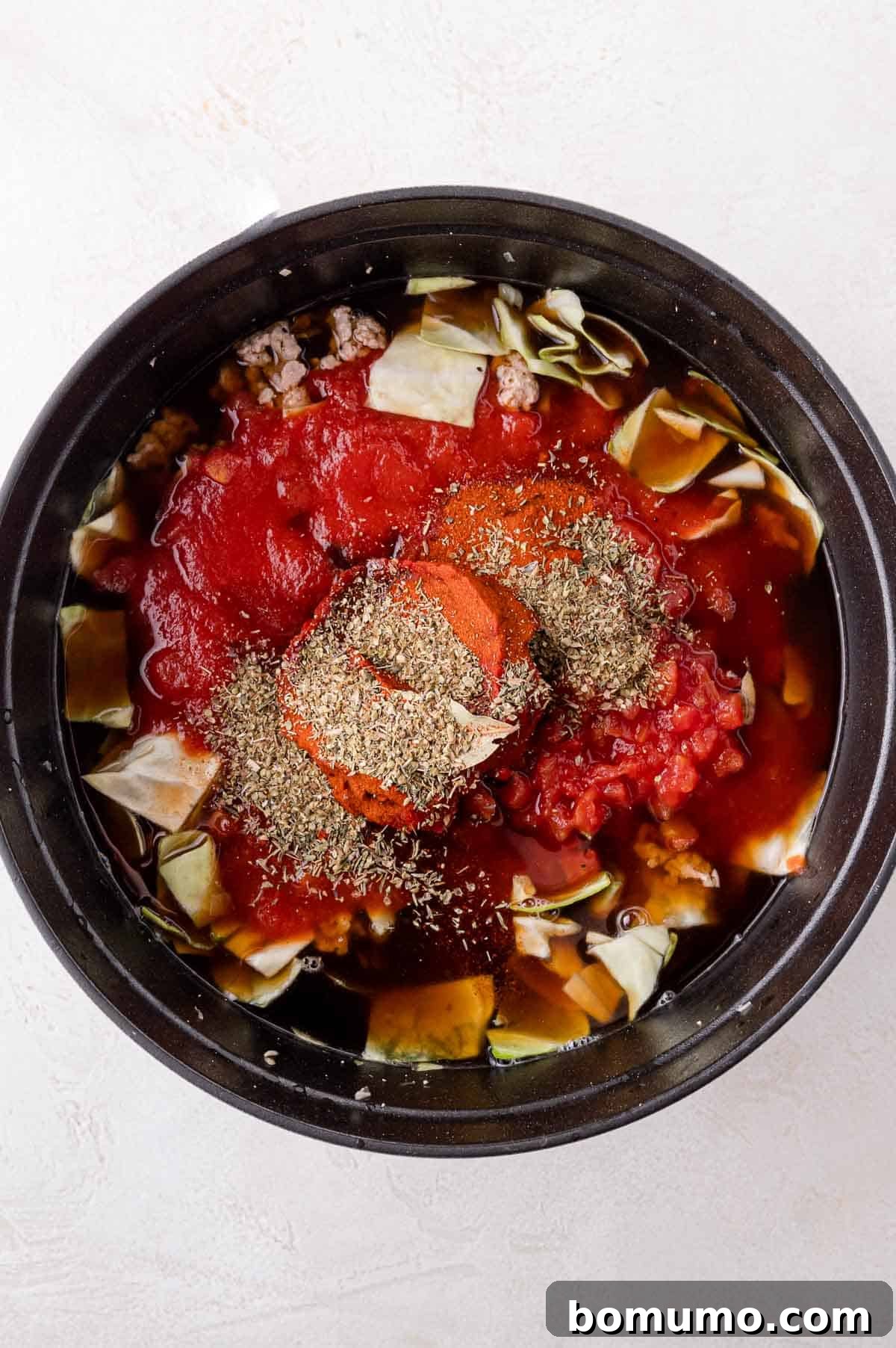 Deconstructed Cabbage Roll Soup 9 A large pot brimming with a rich blend of tomato sauce, tender diced cabbage, juicy diced tomatoes, savory ground meat, and an array of fragrant herbs, meticulously arranged and ready to begin simmering into a comforting soup.