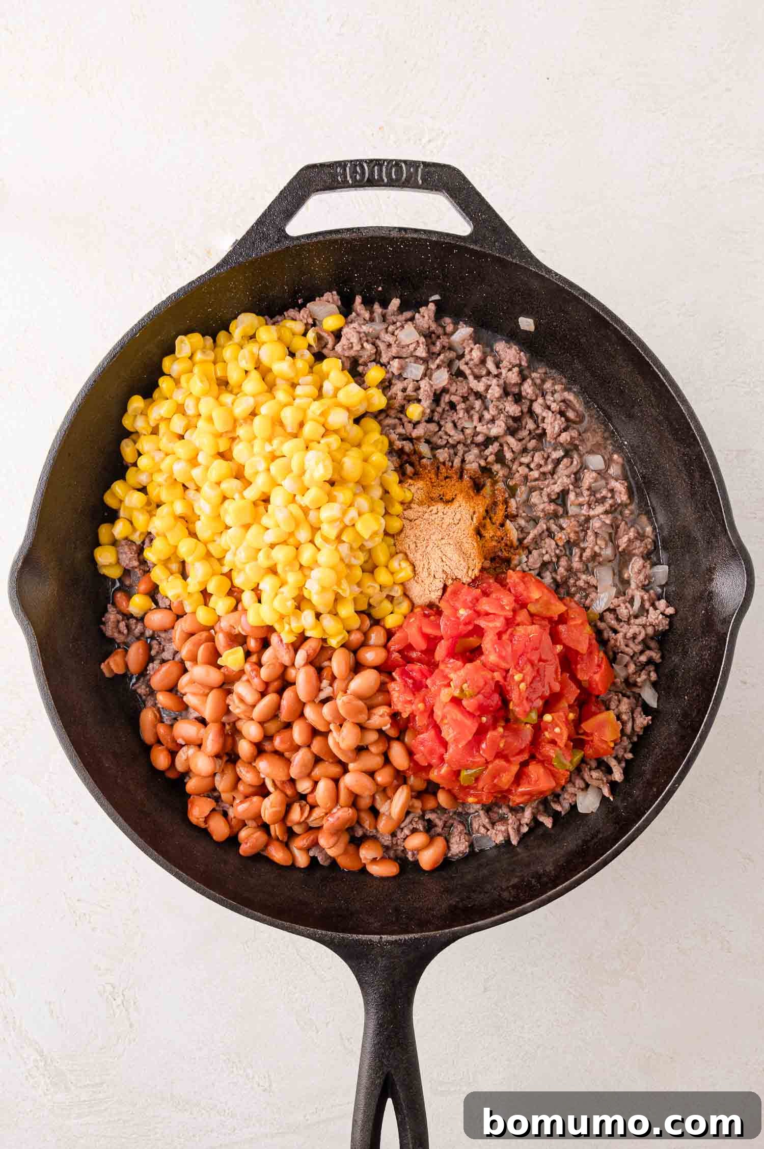 Crunchy Taco Casserole 6 Skillet with cooked ground beef, bright yellow corn kernels, diced tomatoes, tender pinto beans, and a sprinkle of seasoning, all ready to be stirred together. This vibrant mix forms the core of the Walking Taco Casserole filling.