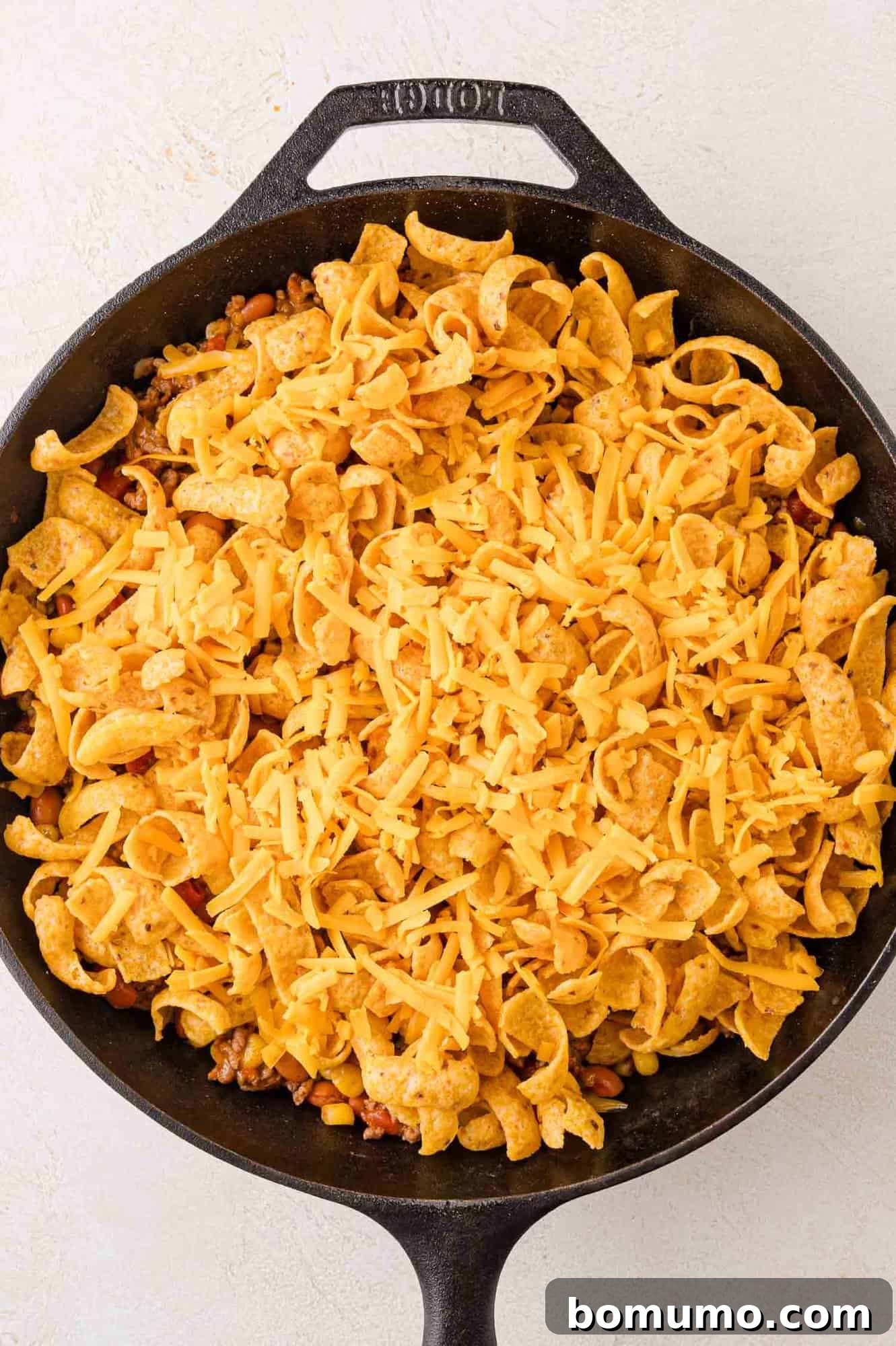Crunchy Taco Casserole 9 A skillet filled with corn chips, beautifully arranged and topped with shredded cheese, all resting on a light-colored surface. This layer is crucial for the signature crunch of the Walking Taco Casserole.